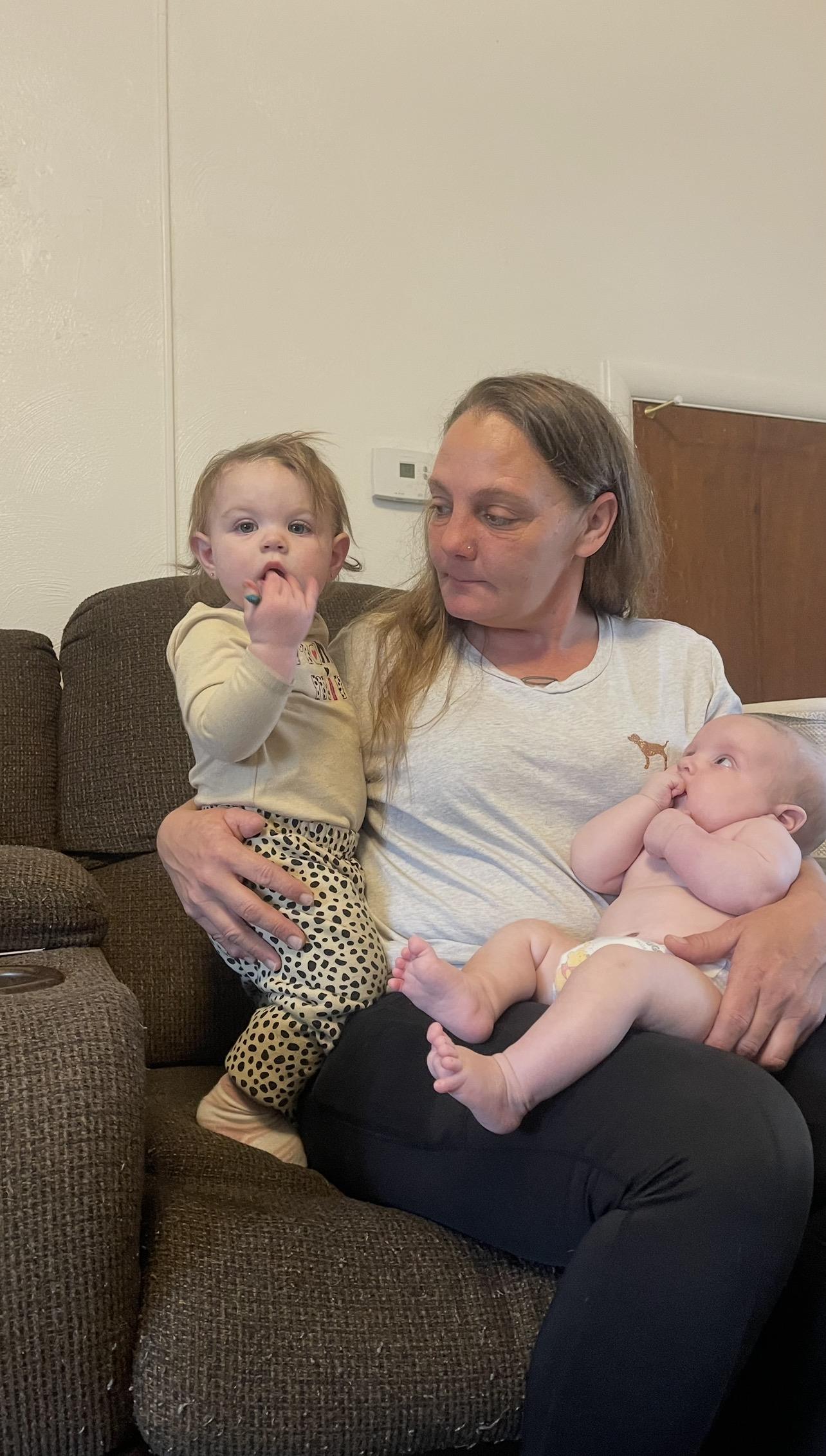 A woman holding a baby and a baby sitting on a couch