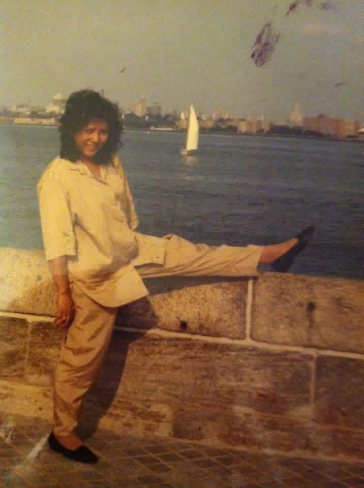 A woman standing on a stone wall with a sailboat in the background