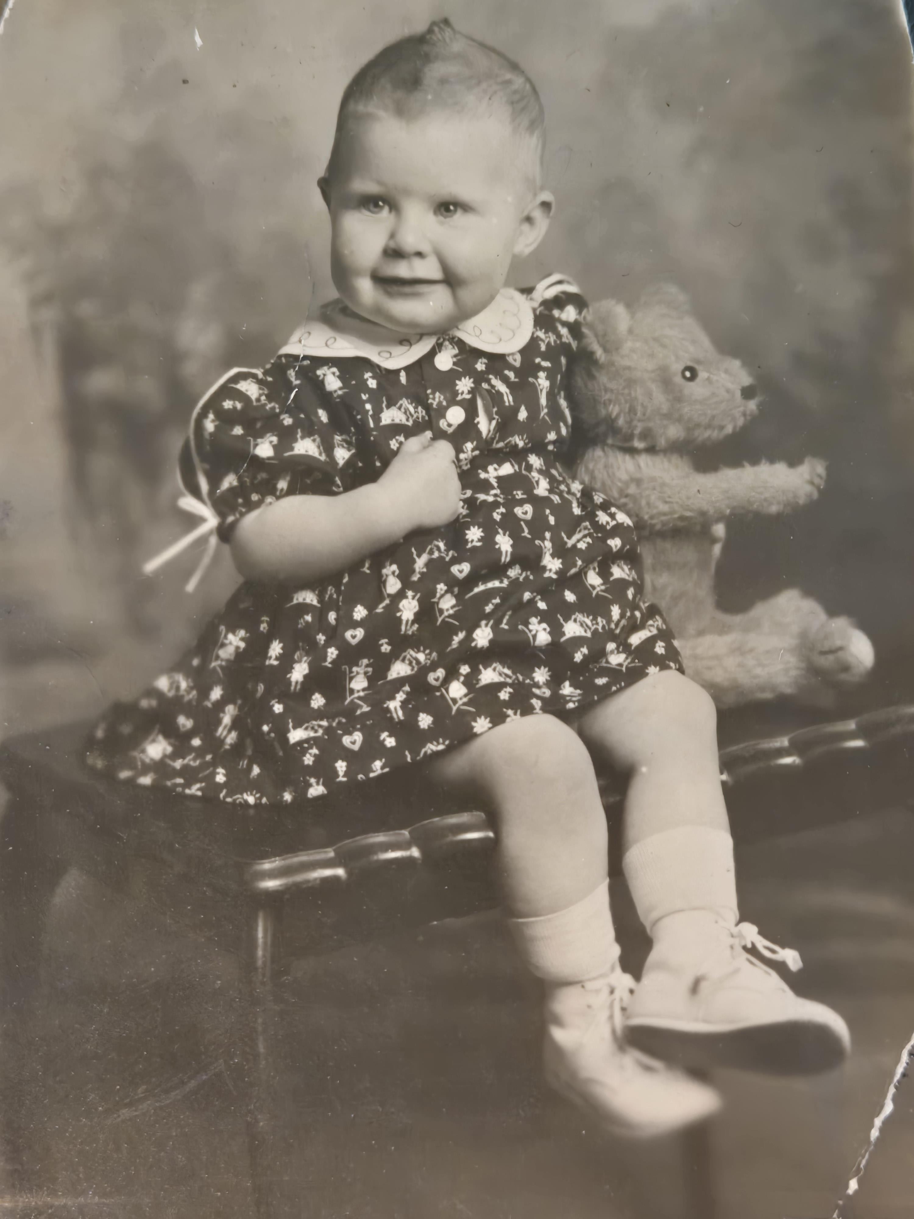 A baby sitting on a chair holding a teddy bear