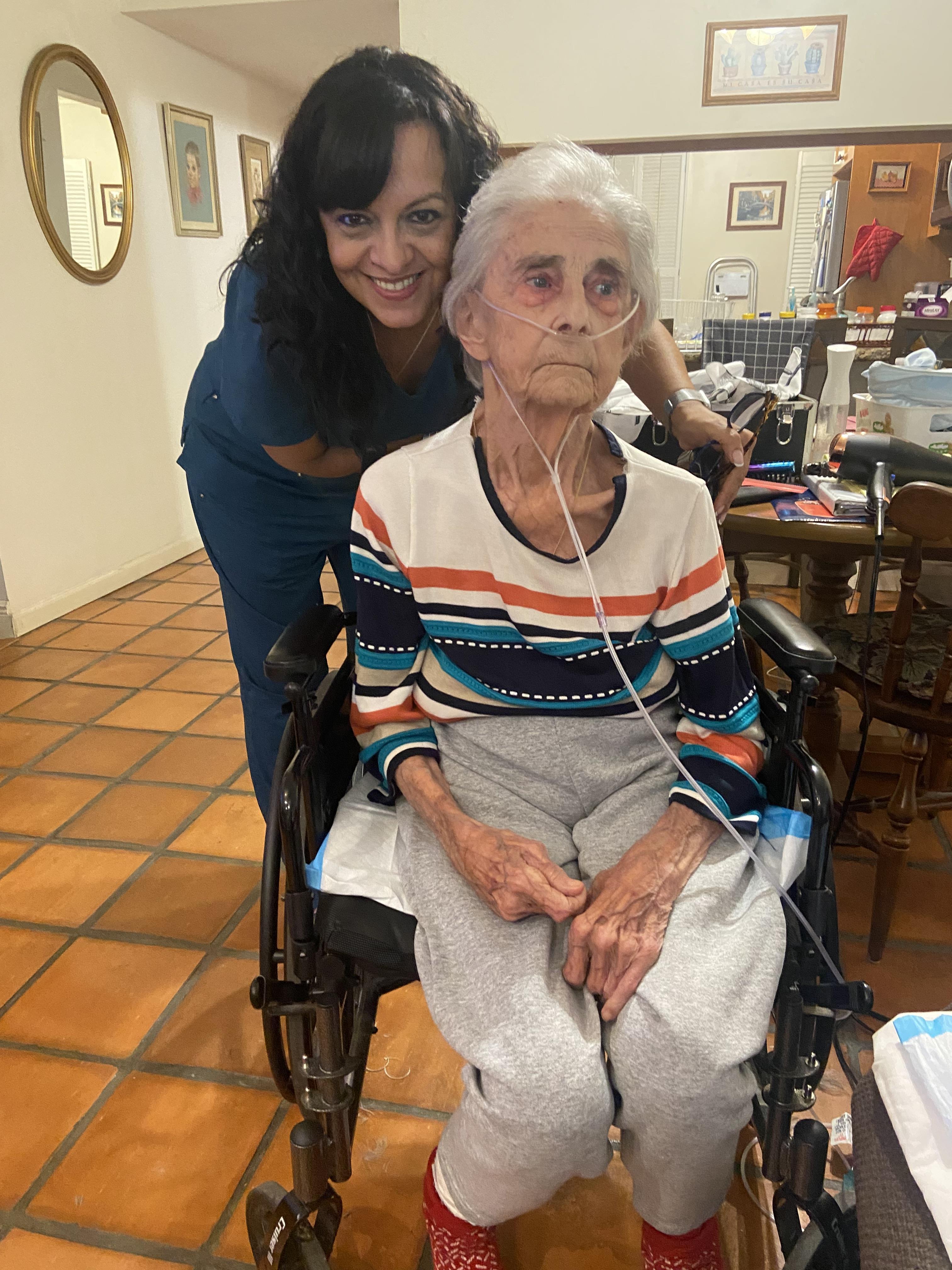 A woman standing next to an old woman in a wheelchair