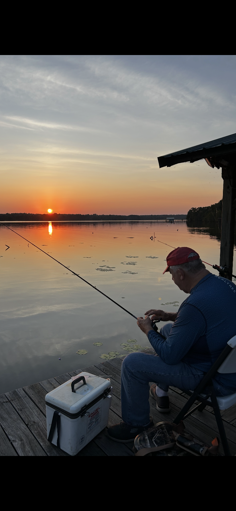 A man sitting on a dock fishing at sunset