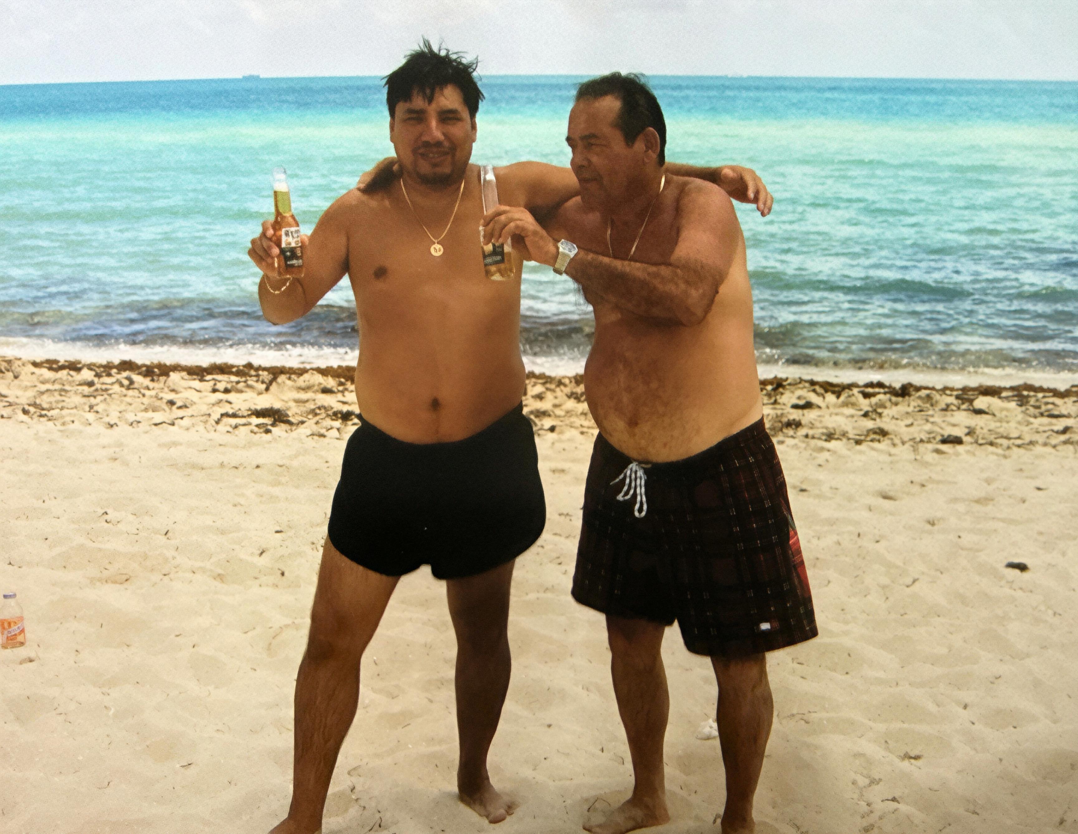Two men standing on a beach holding bottles of beer