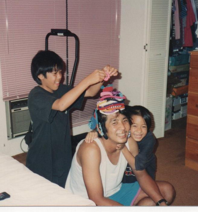 A man sitting on the floor with a boy holding a stack of socks on his head