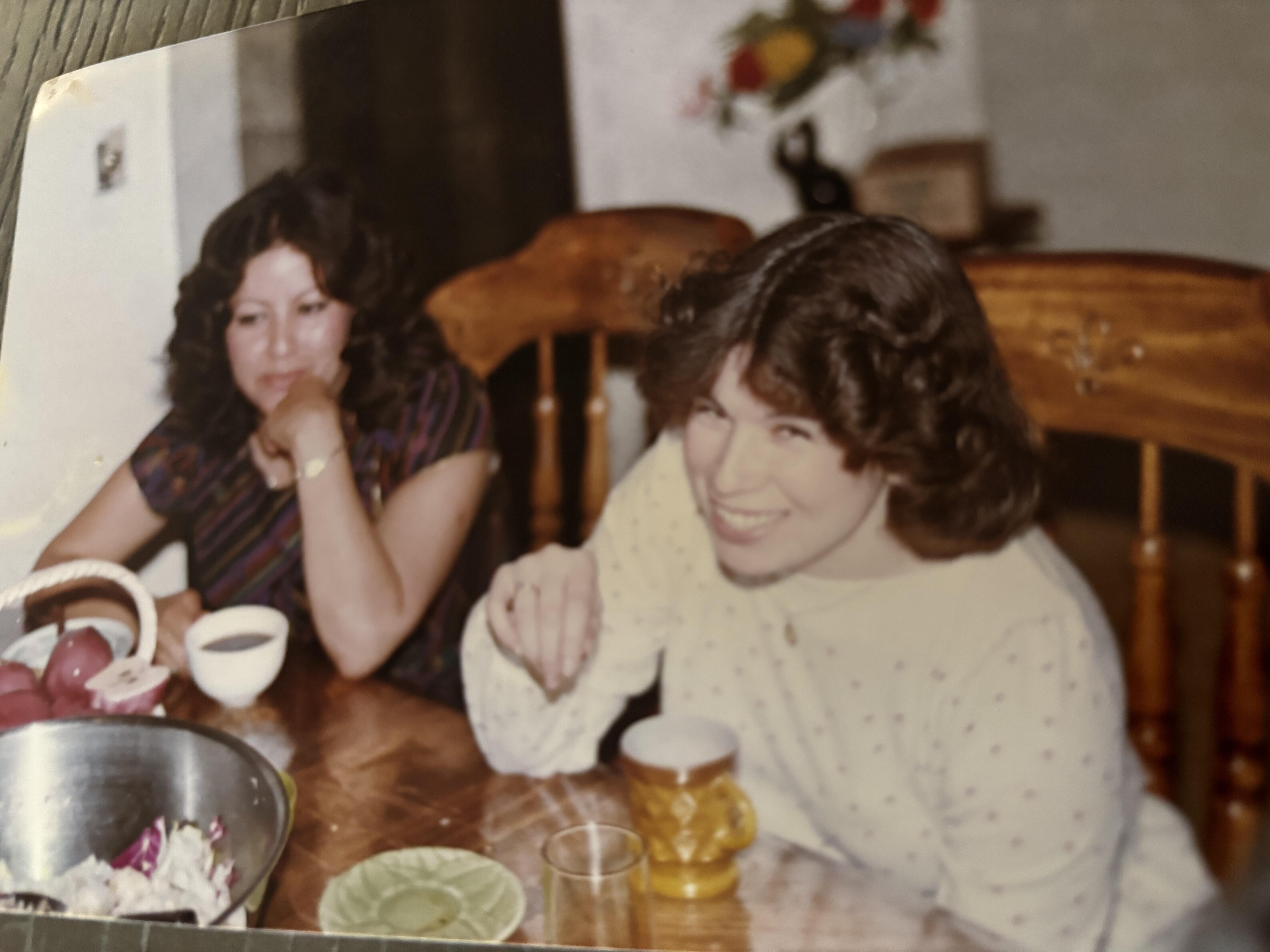 A woman sitting at a table with a woman smiling