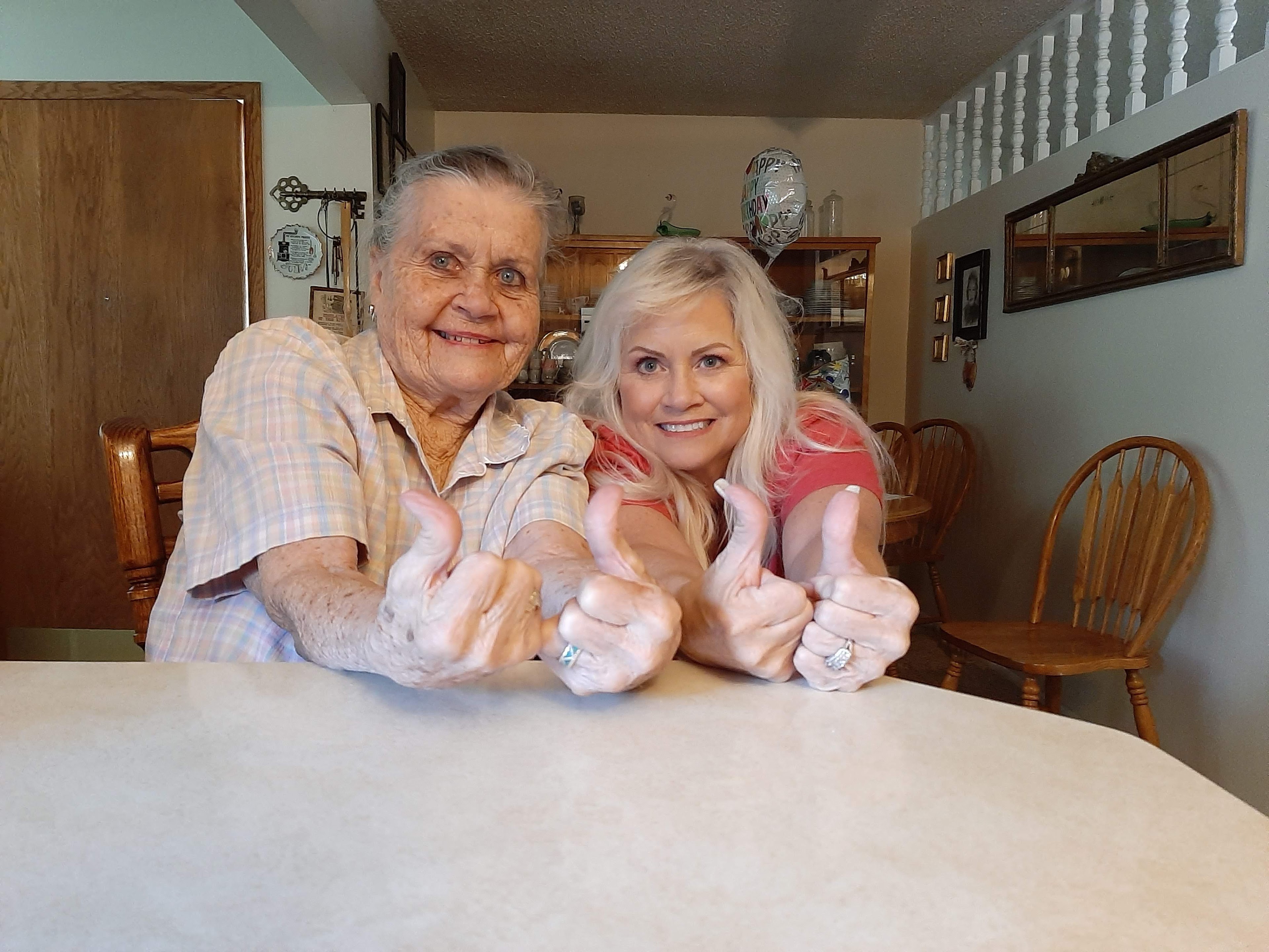 Two women sitting at a table with thumbs up