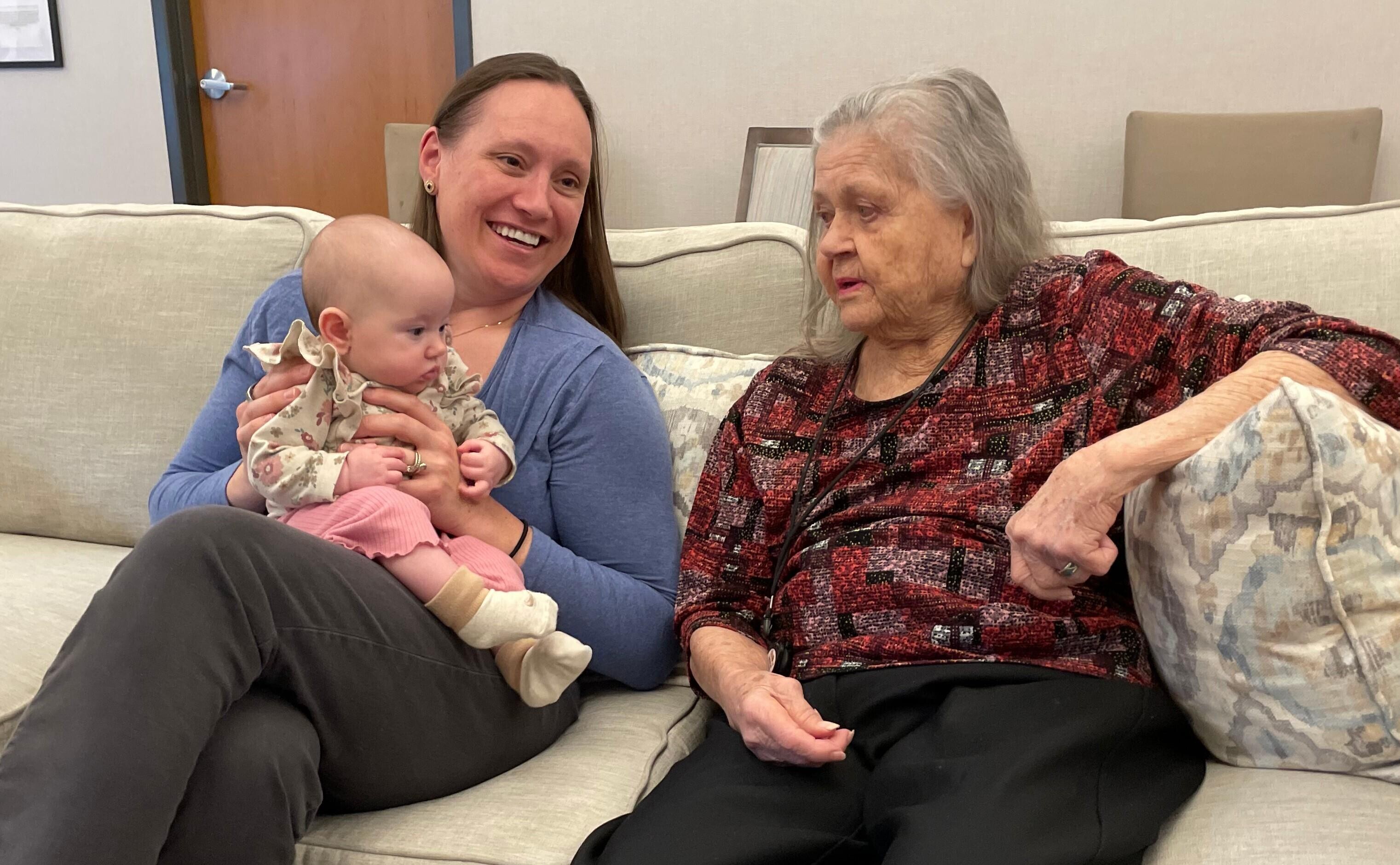 A woman holding a baby and a woman sitting on a couch