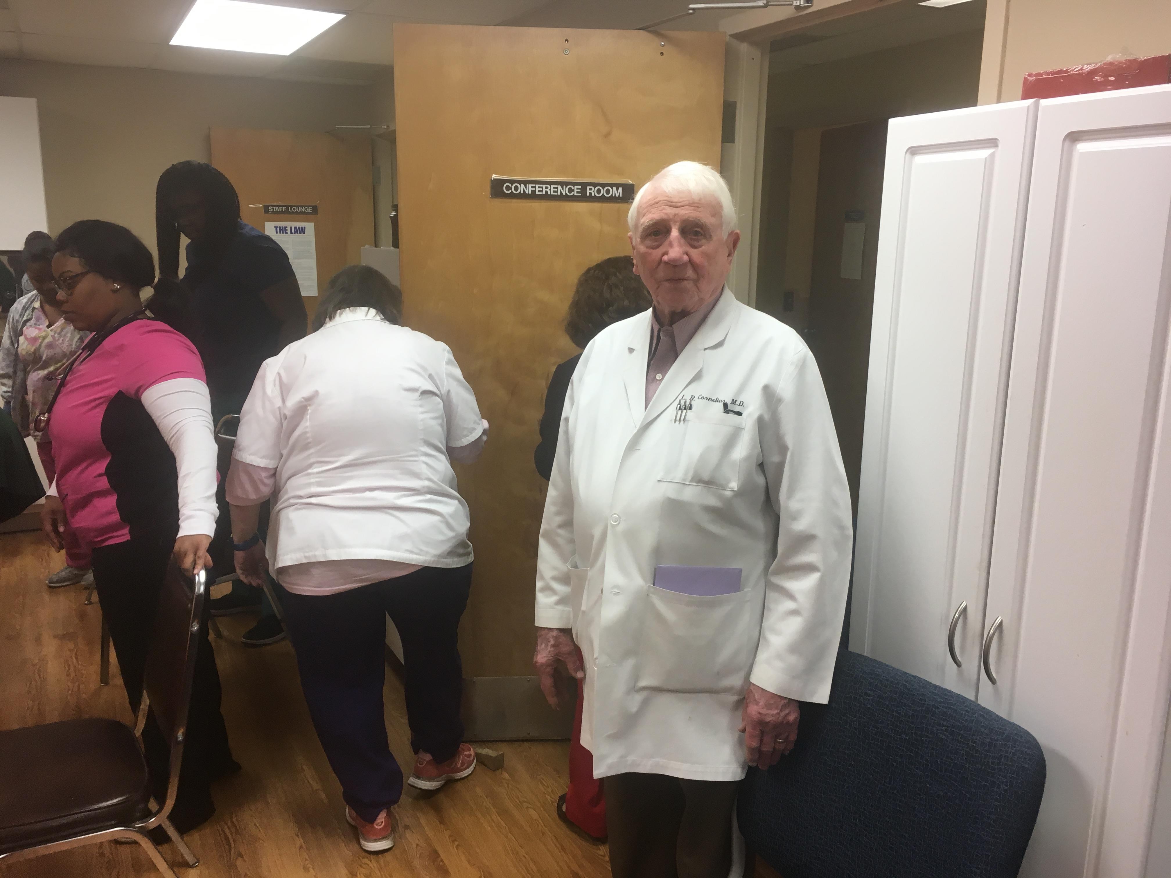 A man in a white coat standing in a room with other people