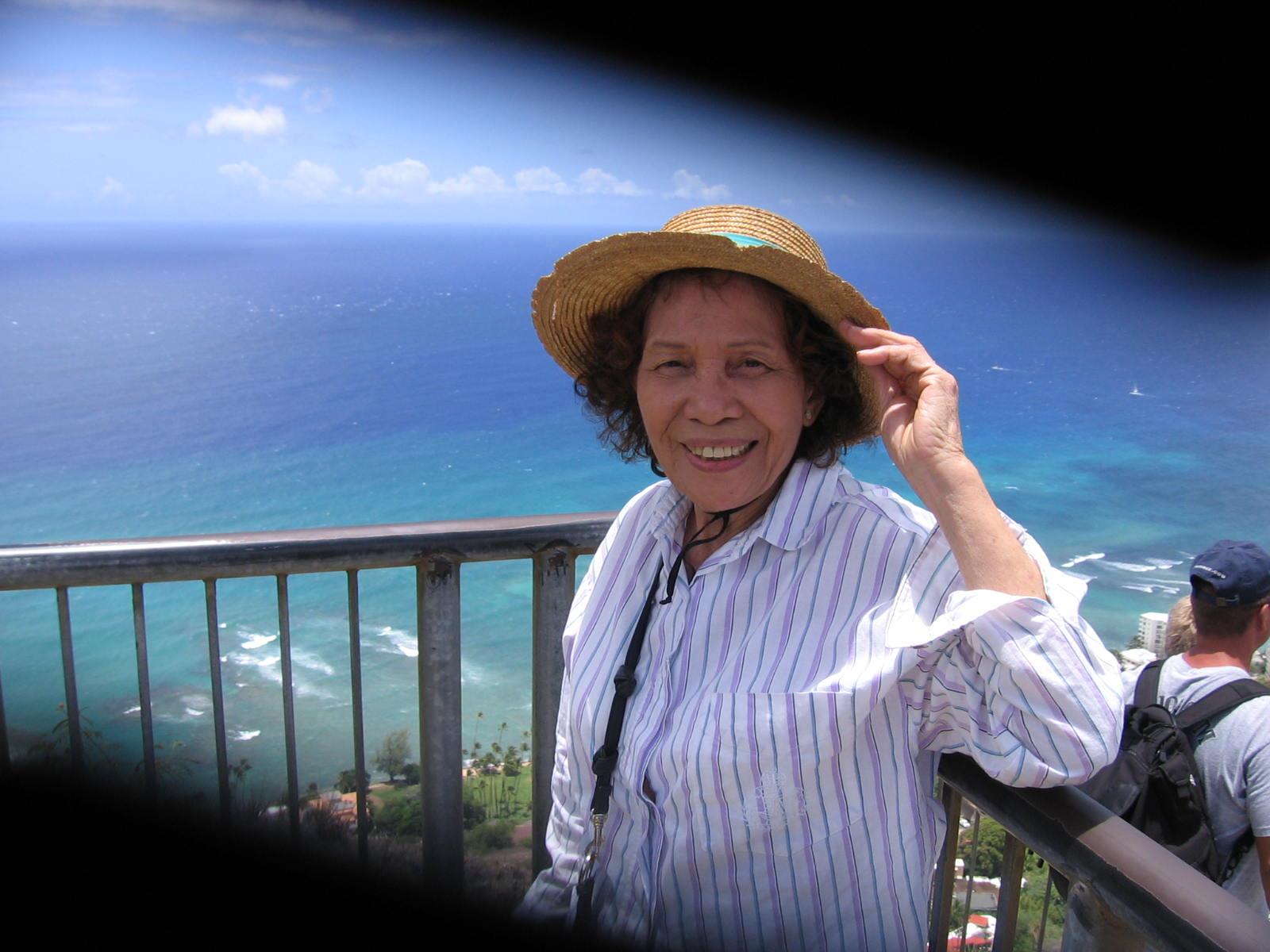 A woman wearing a hat and standing on a balcony overlooking the ocean