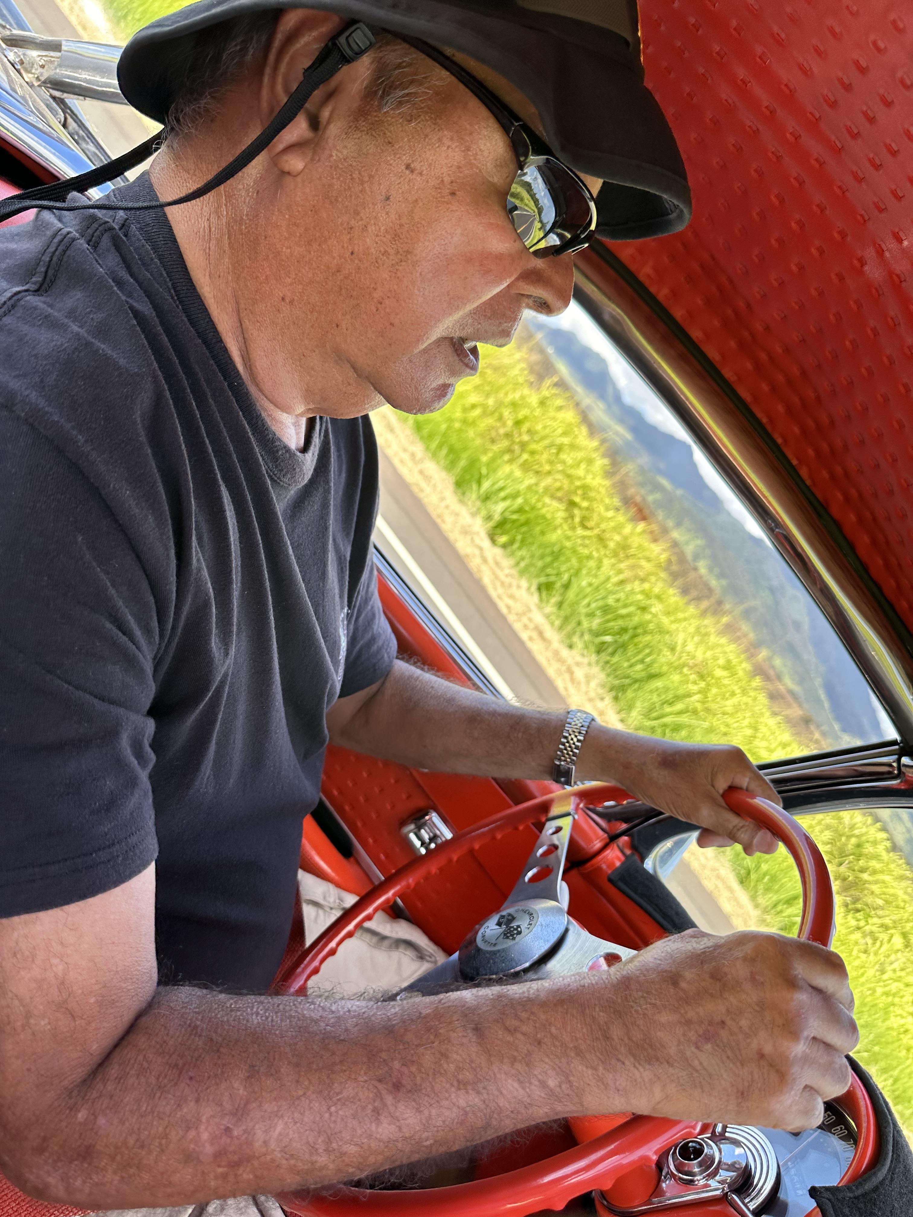 A man in a black hat and sunglasses holding a red steering wheel