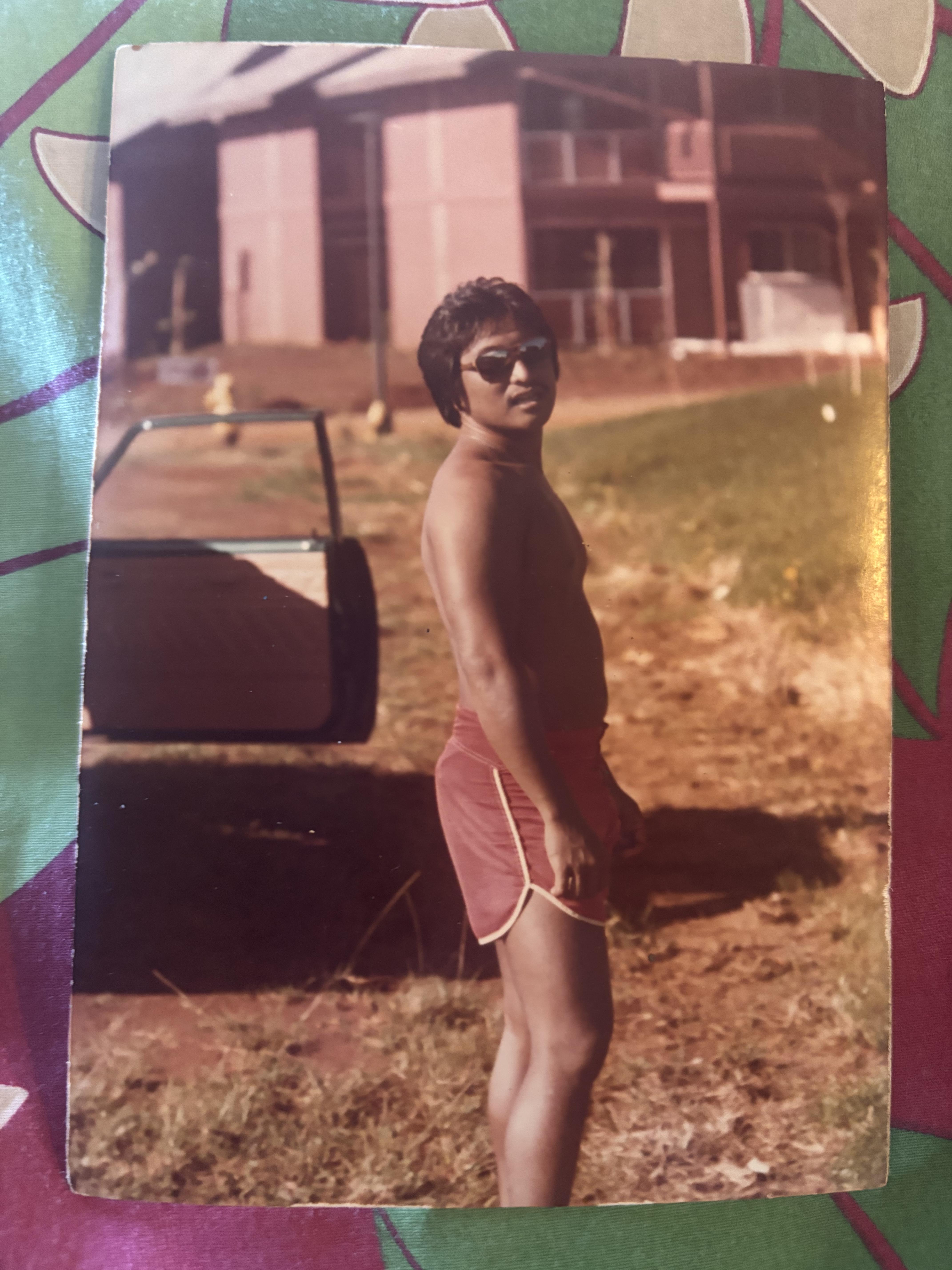 A man in shorts and sunglasses standing in front of a car