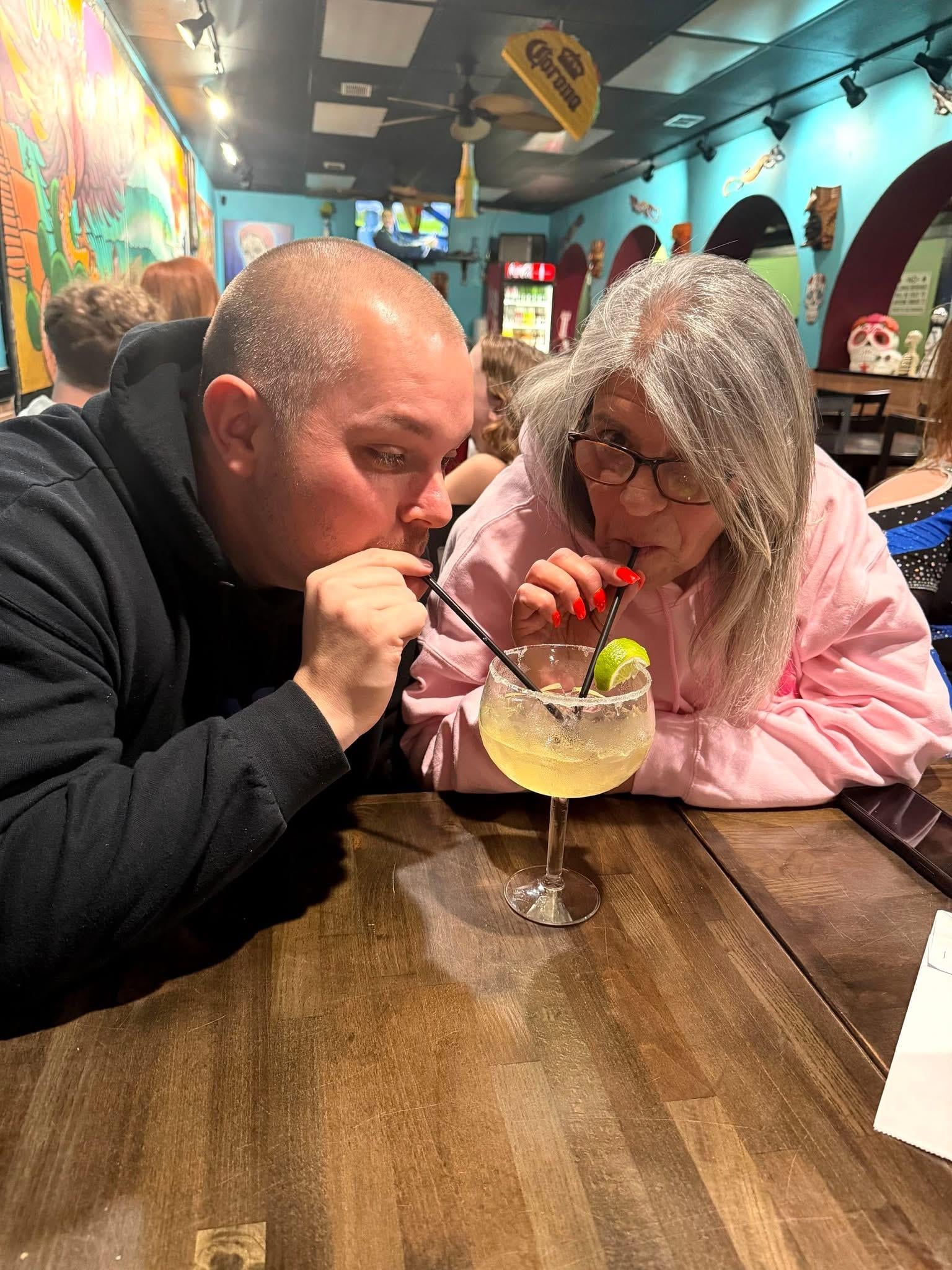 A man and woman sitting at a table drinking from straws