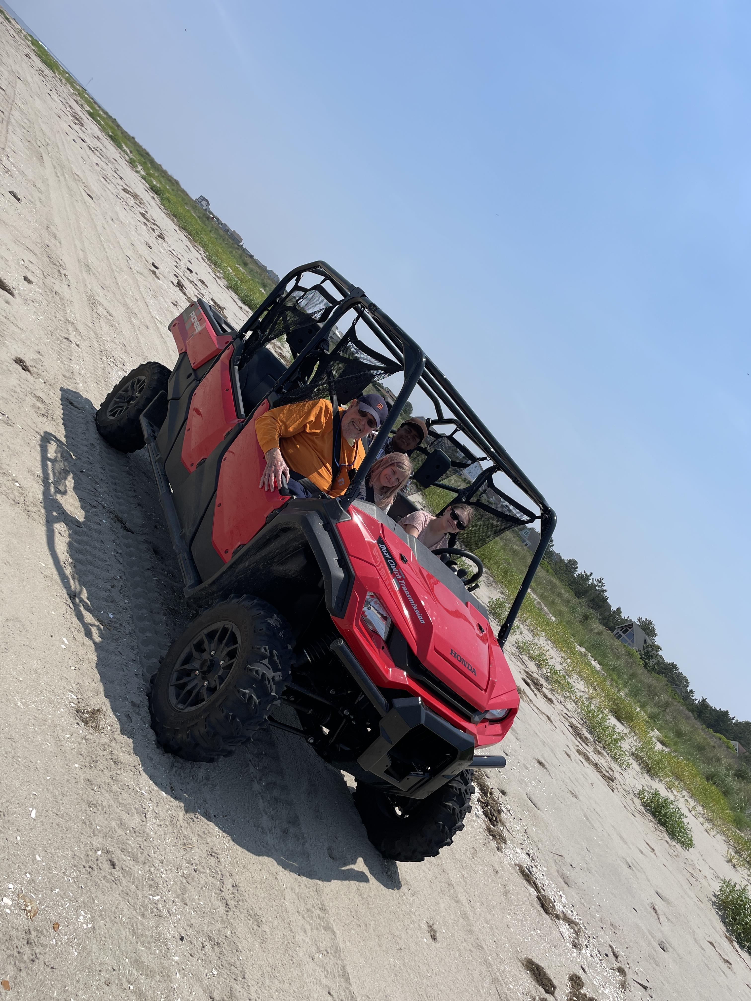 A group of people in a red vehicle on a sandy road