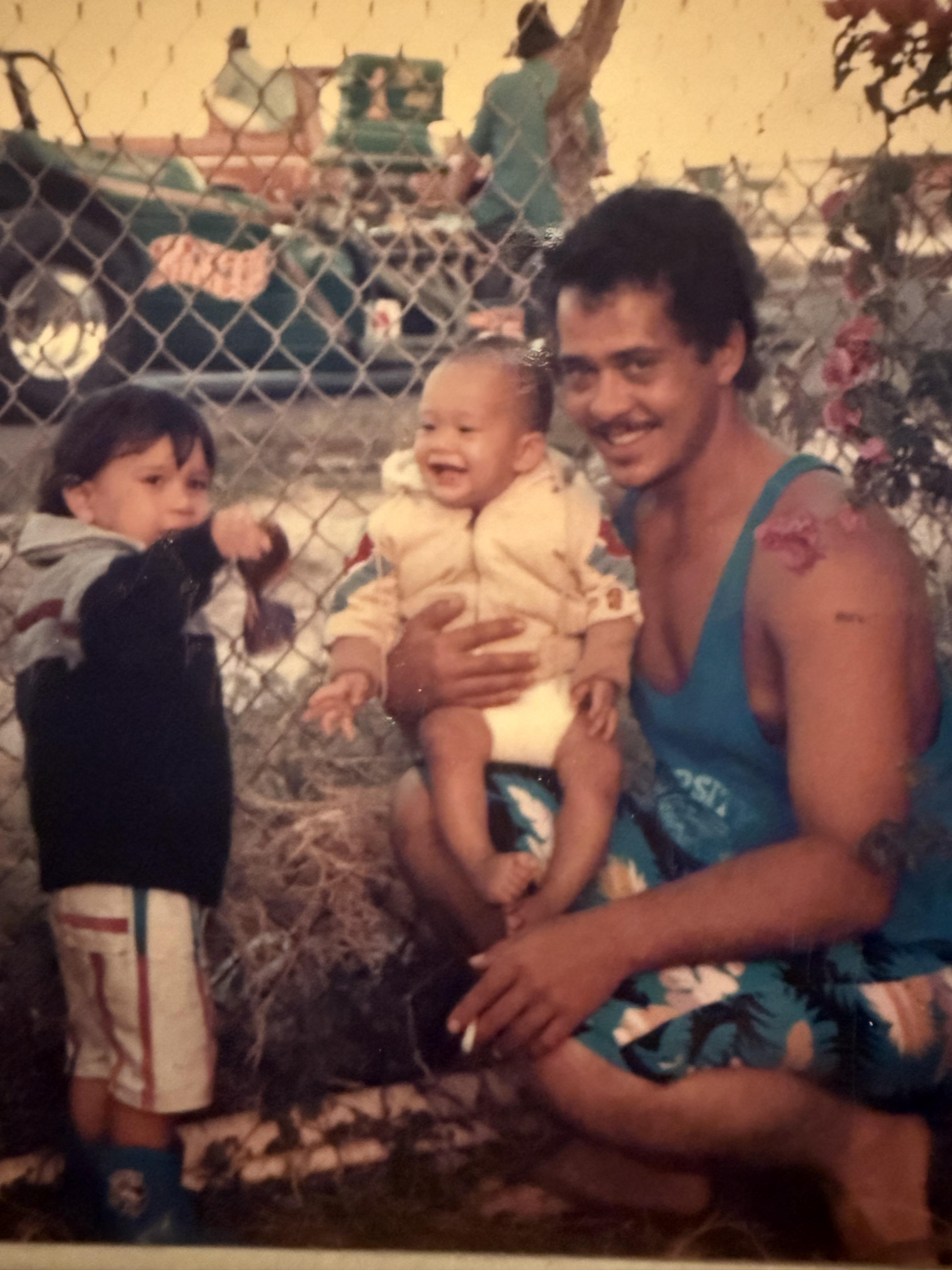 A man holding a baby and a child standing behind a fence