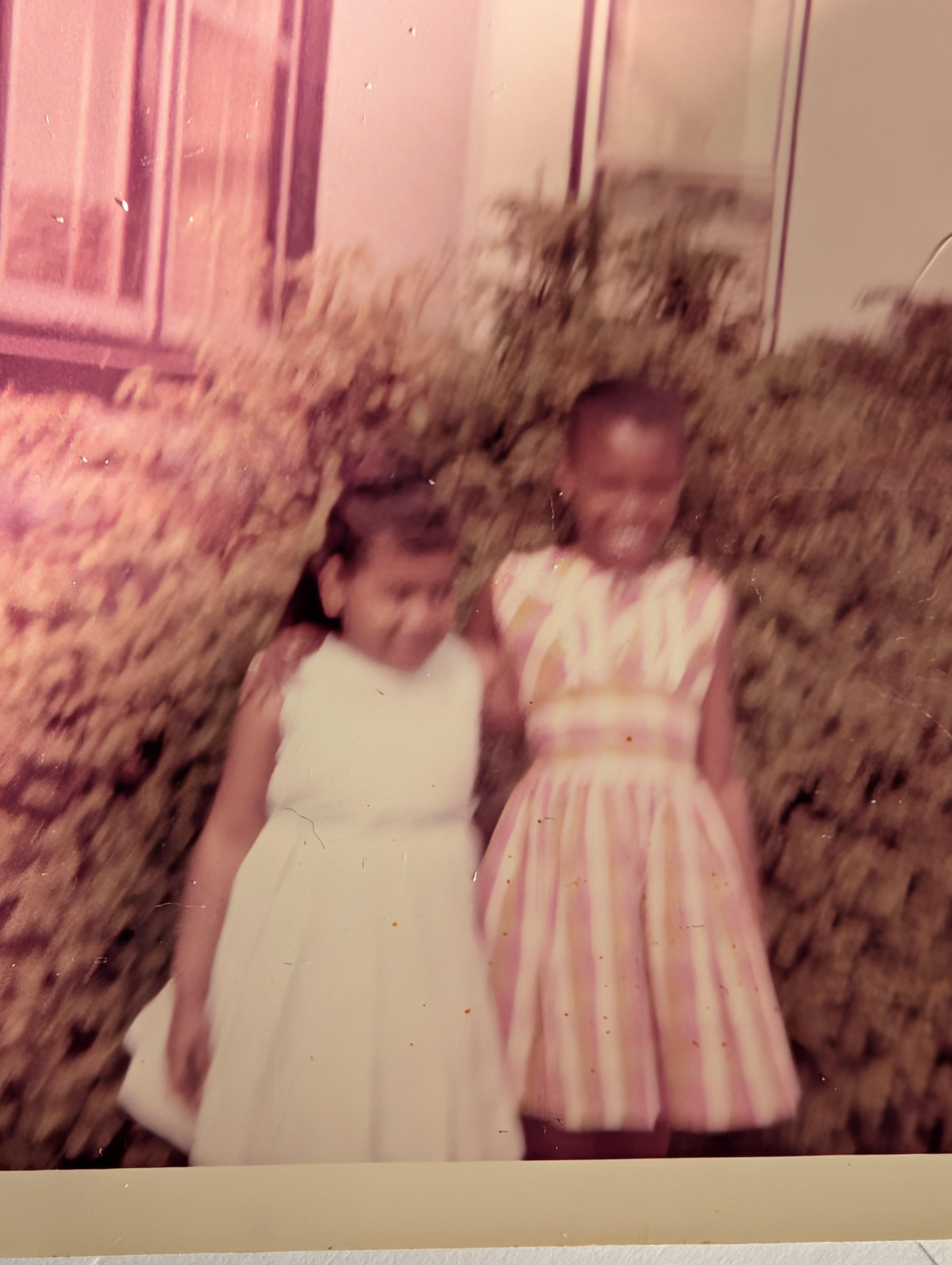 Two girls in dresses standing in front of a bush