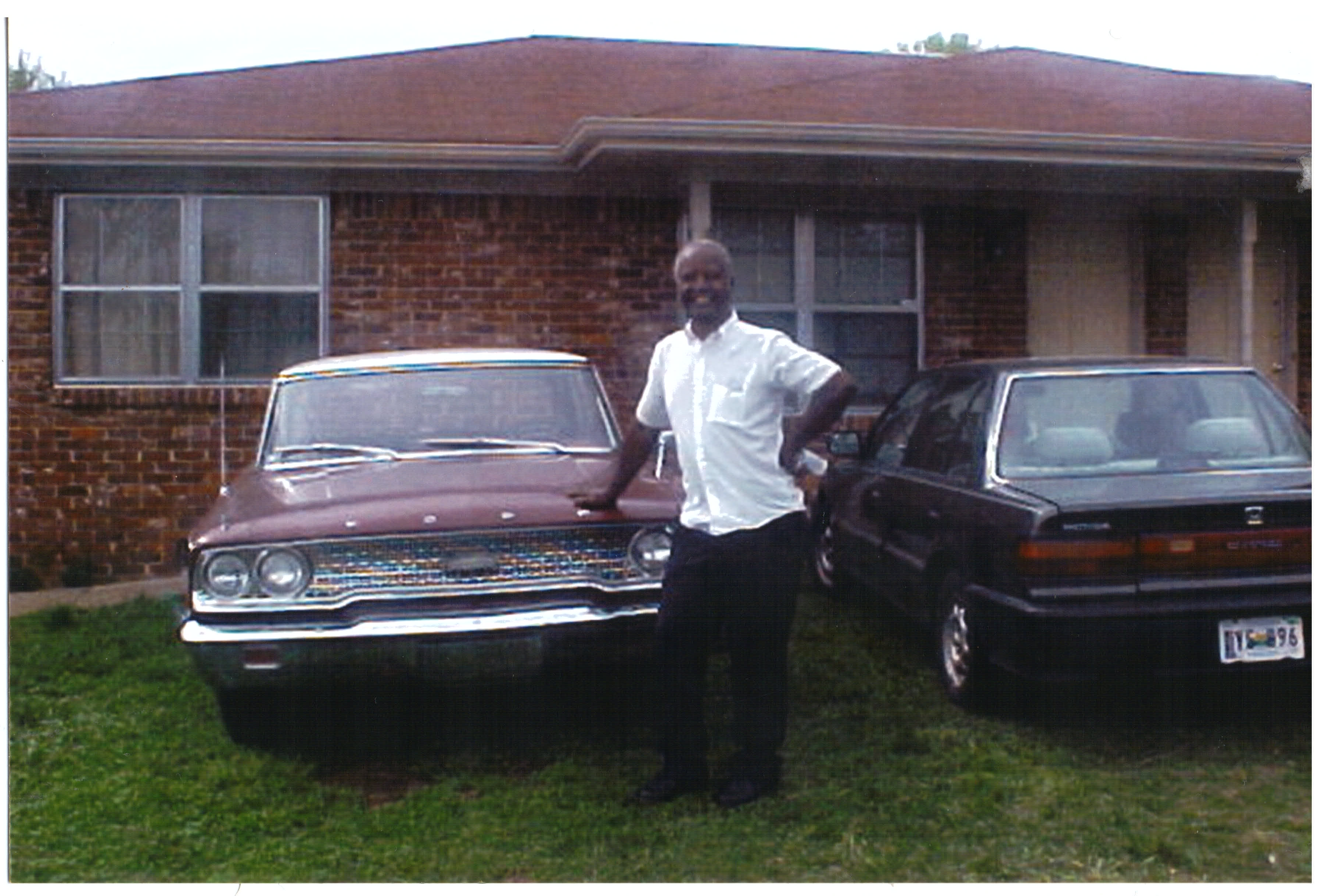 A man standing in front of a house with cars