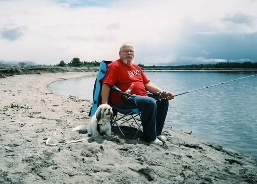 A man sitting in a chair with a dog on the beach