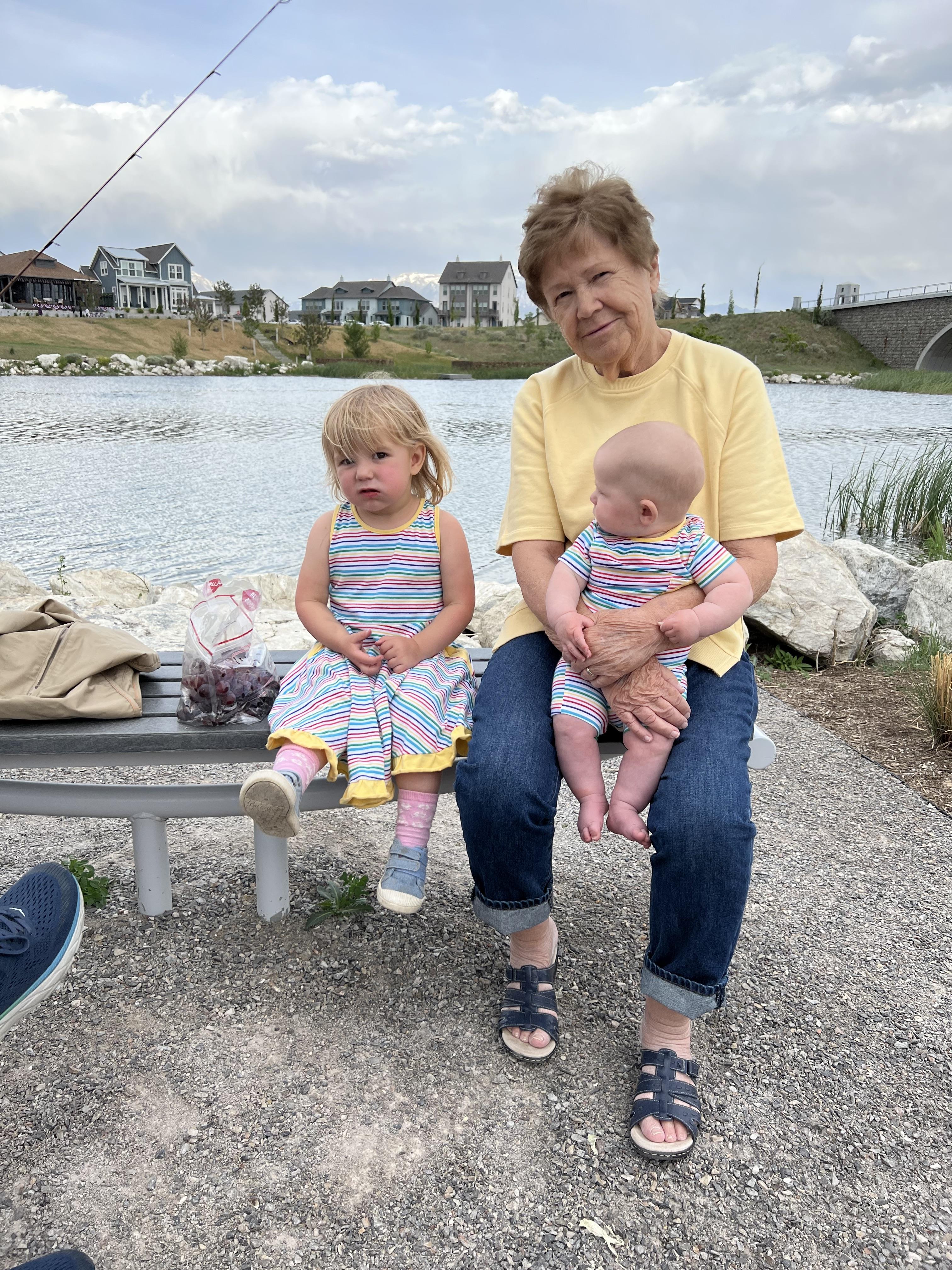 A woman and a baby sitting on a bench by a lake