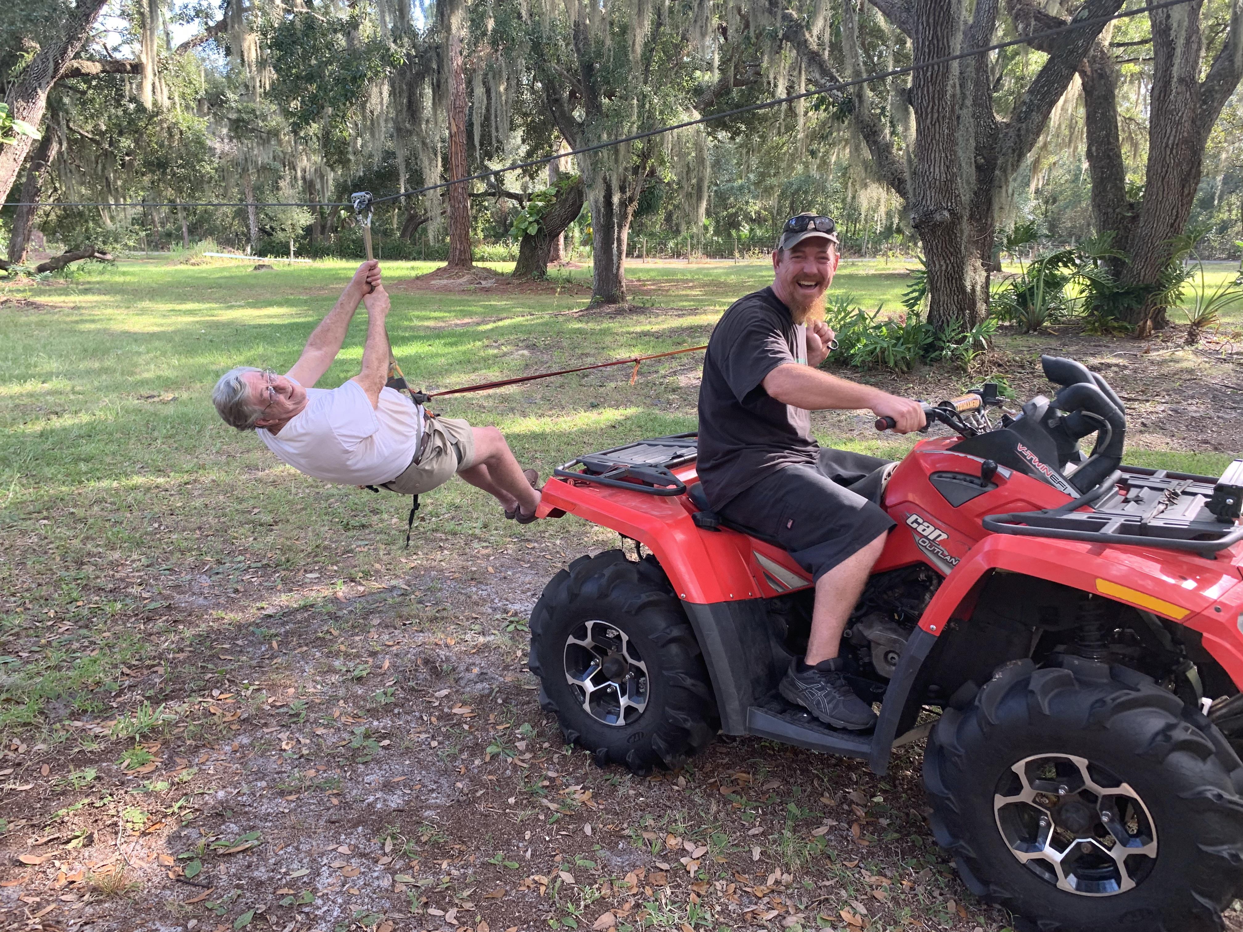 A man on a four wheeler pulling another man on a leash