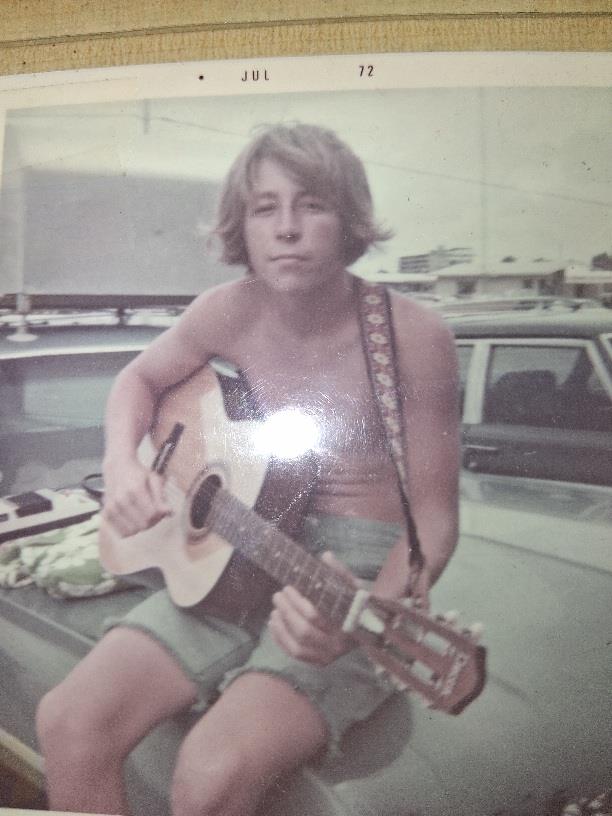 A man sitting on a car holding a guitar