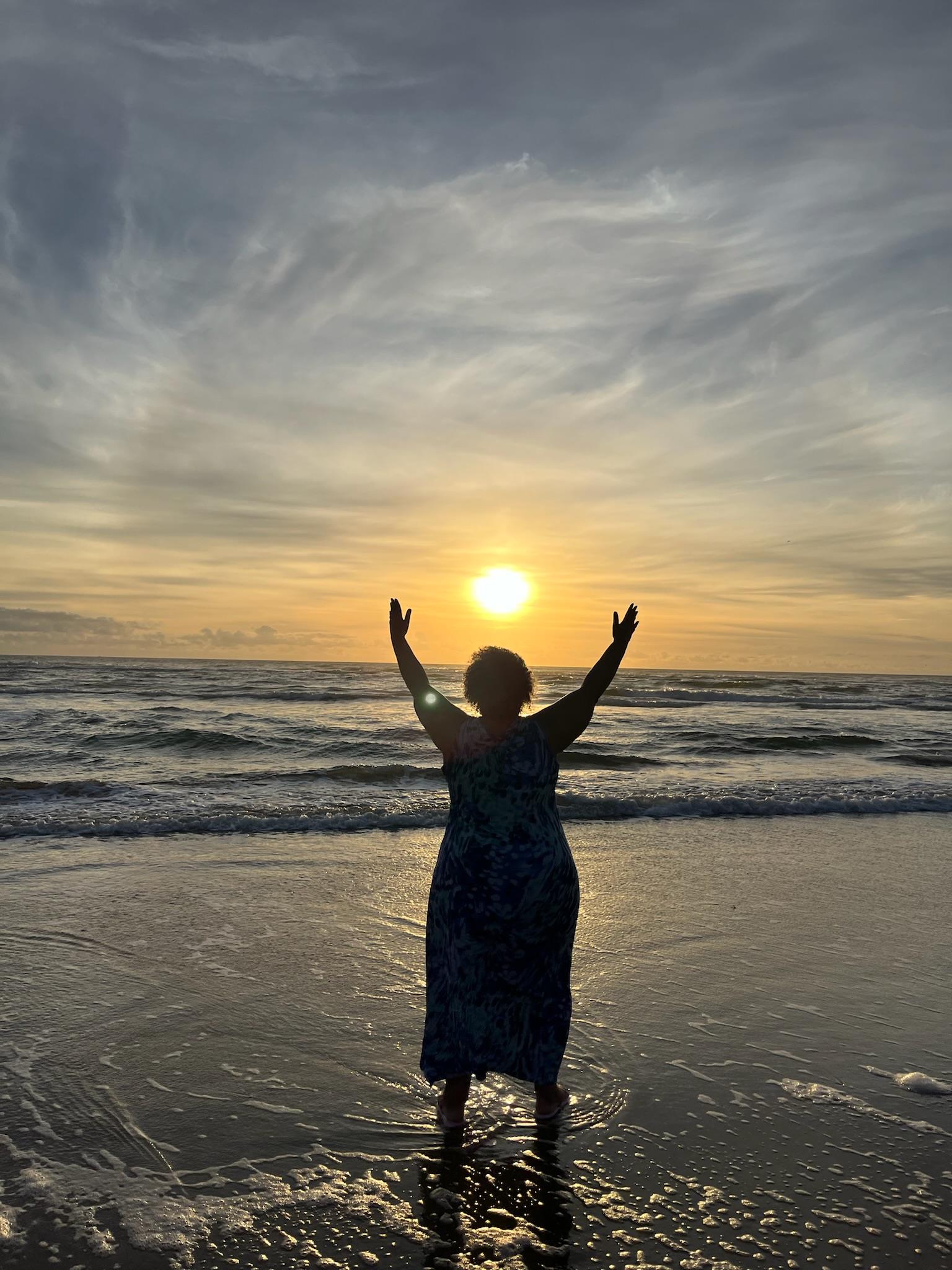 A woman standing on a beach with her arms up