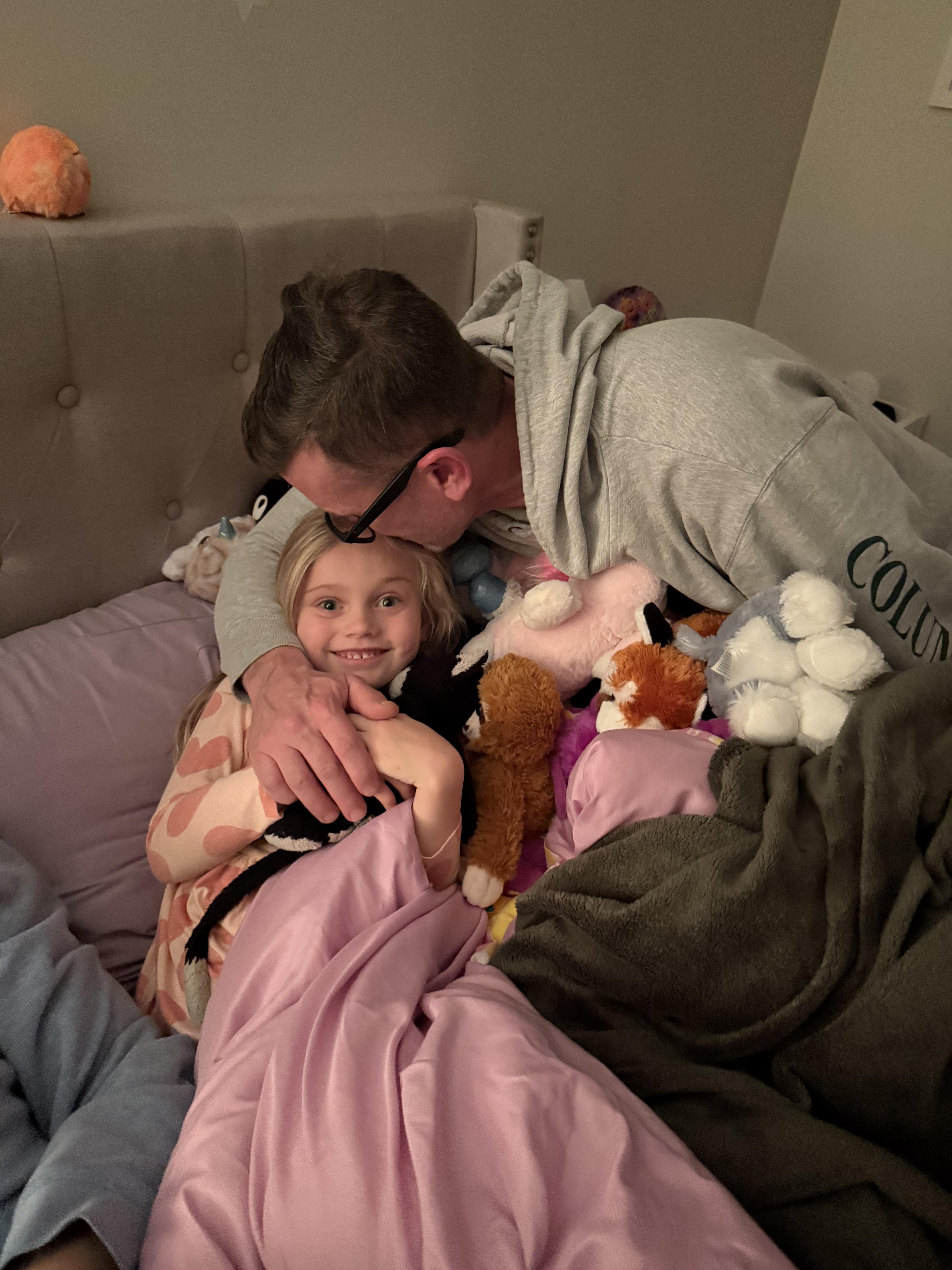 A man and a girl lying on a bed with stuffed animals