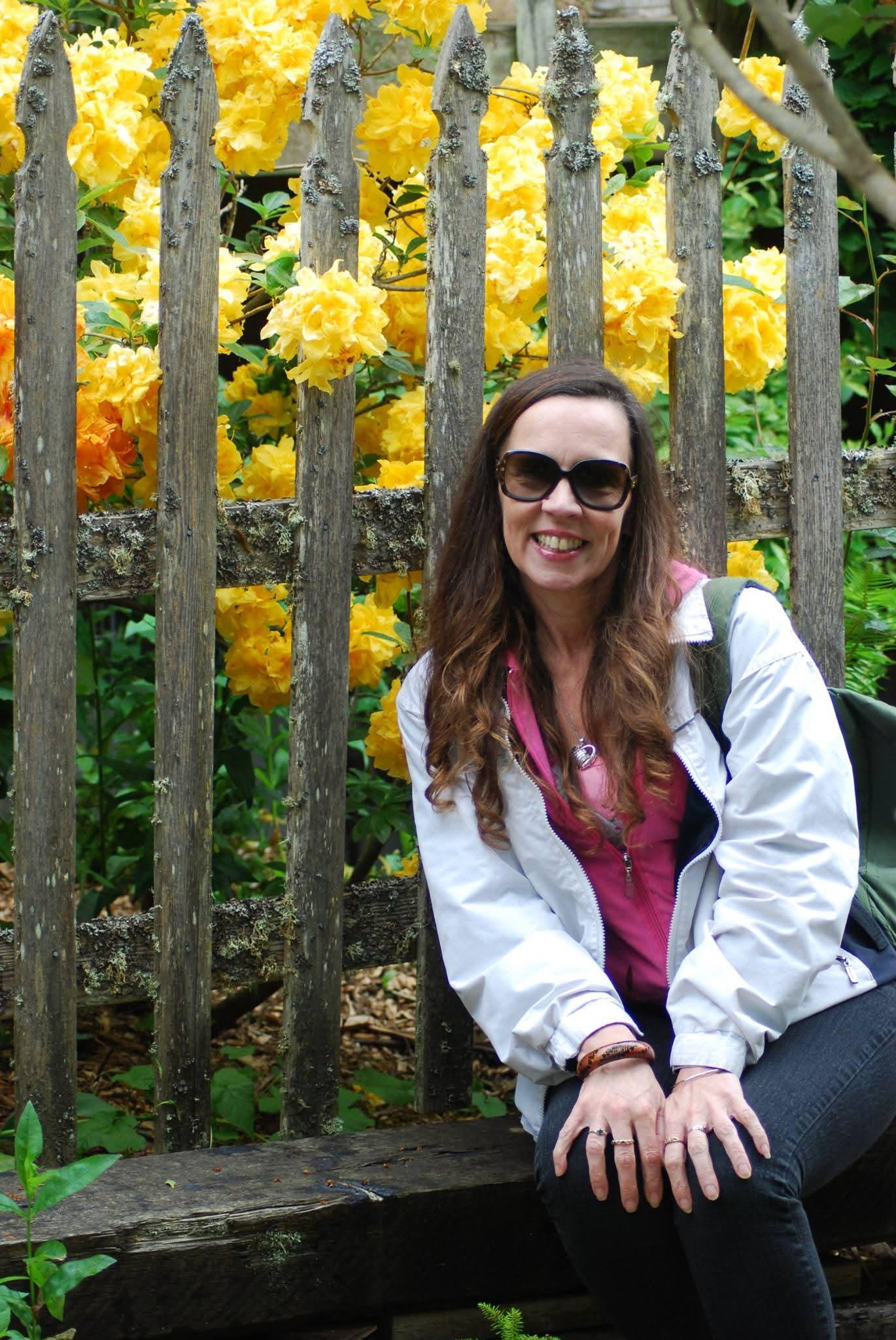 A woman sitting in front of a fence with yellow flowers