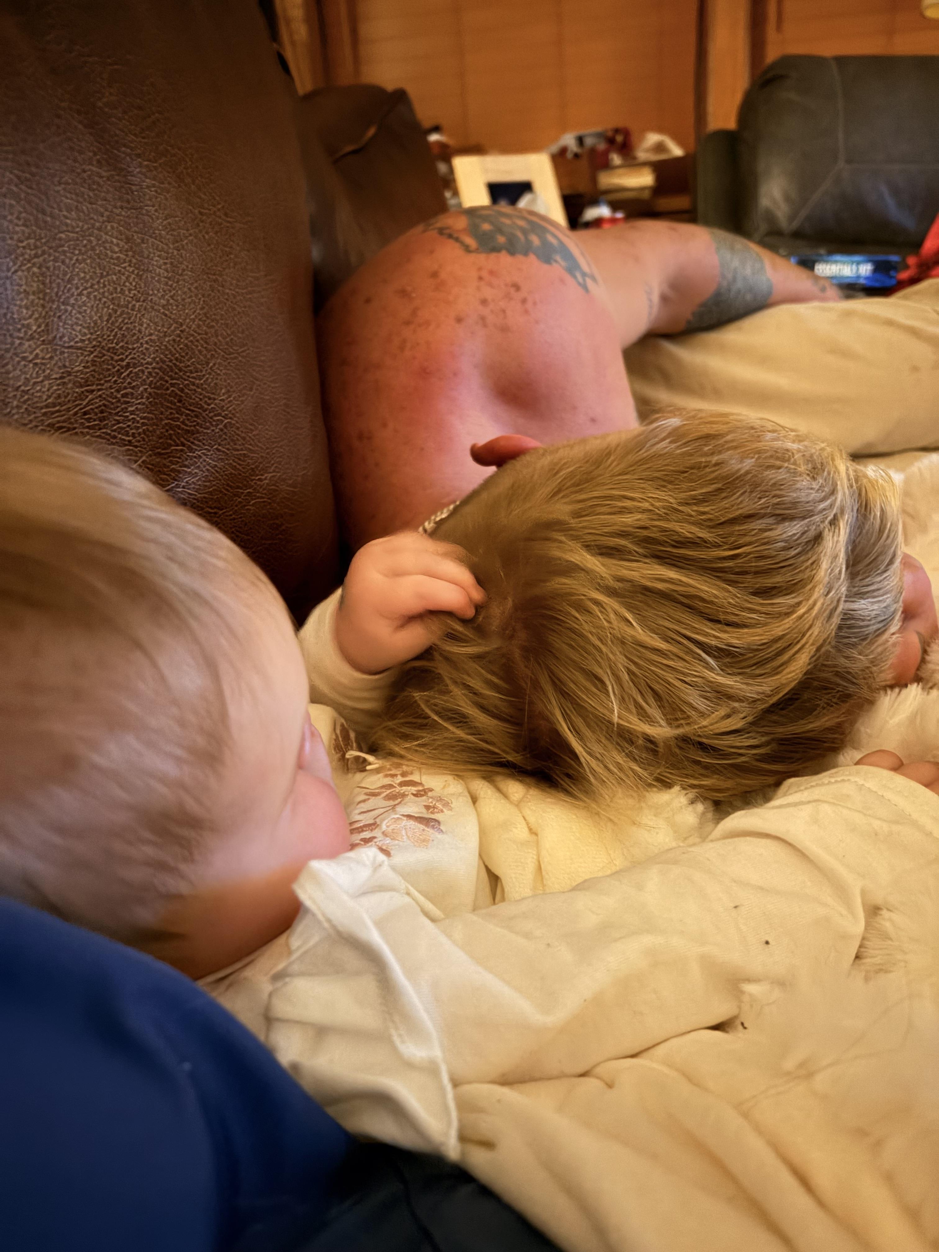 A baby lying on a couch with a man lying on his back