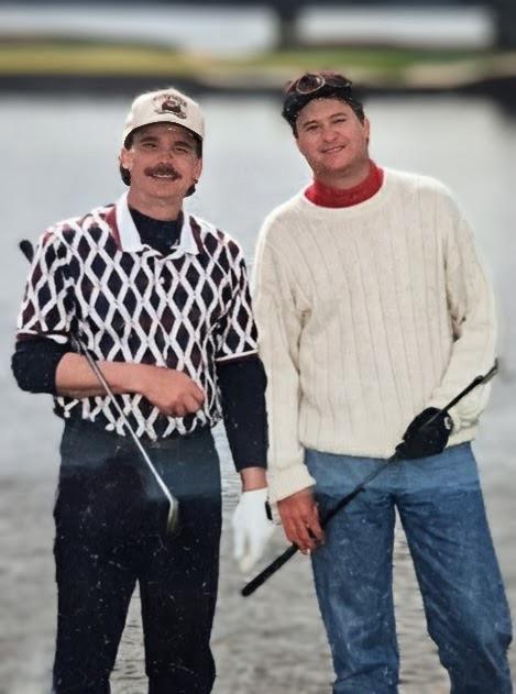 A couple of men standing in water holding golf clubs