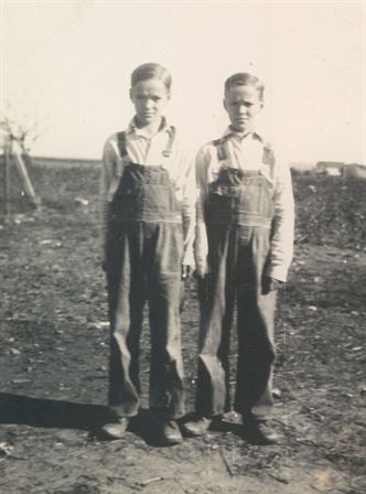 A pair of young boys in overalls standing in a field