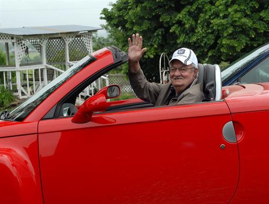 A man in a red convertible car waving