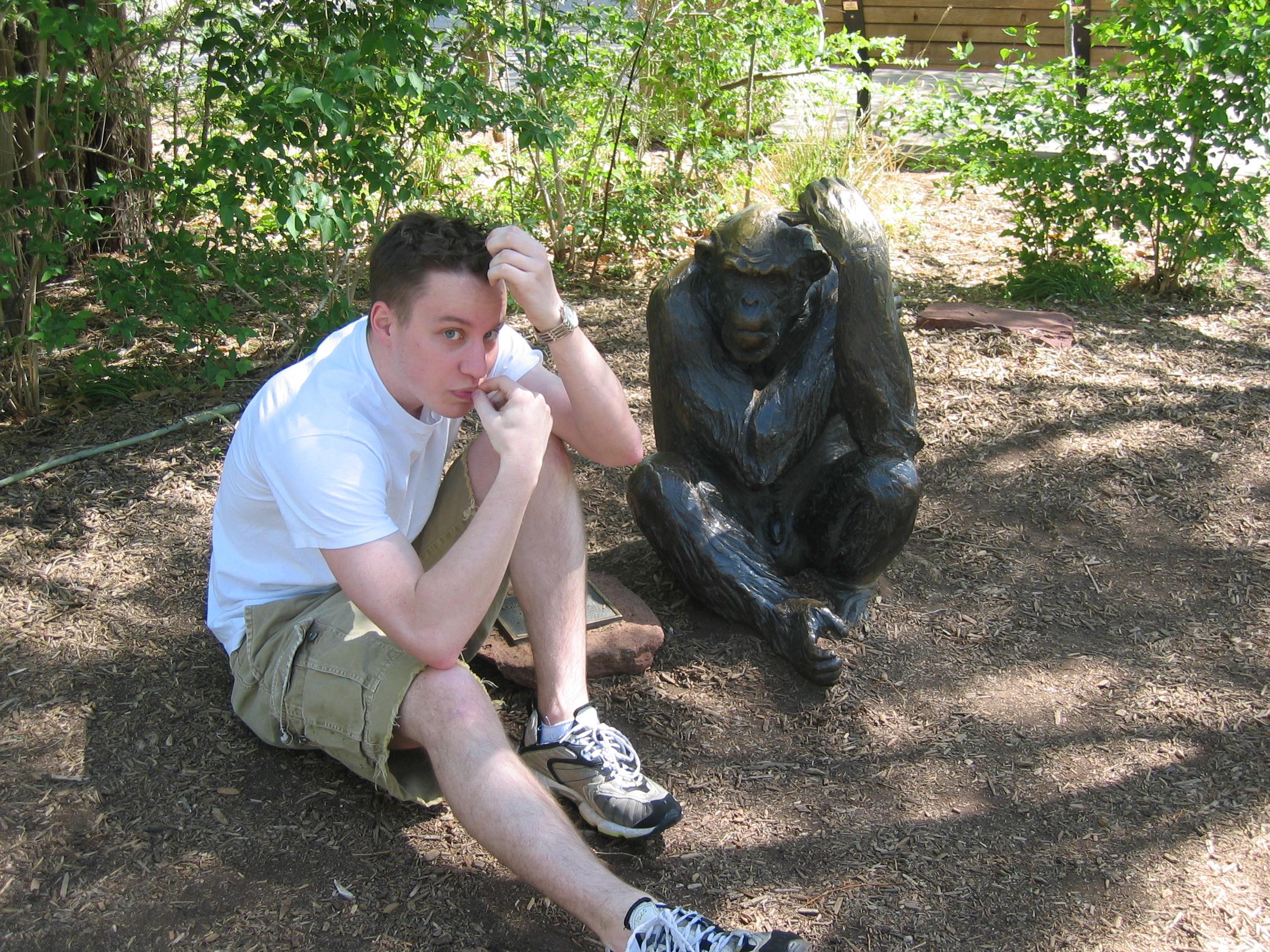 A man sitting next to a statue of a monkey