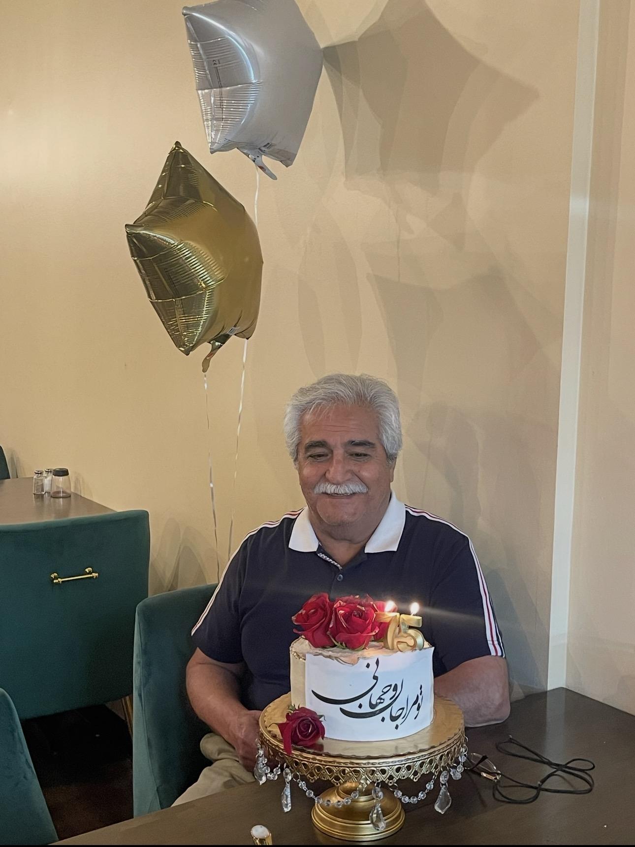 A man sitting in a chair with a cake and balloons