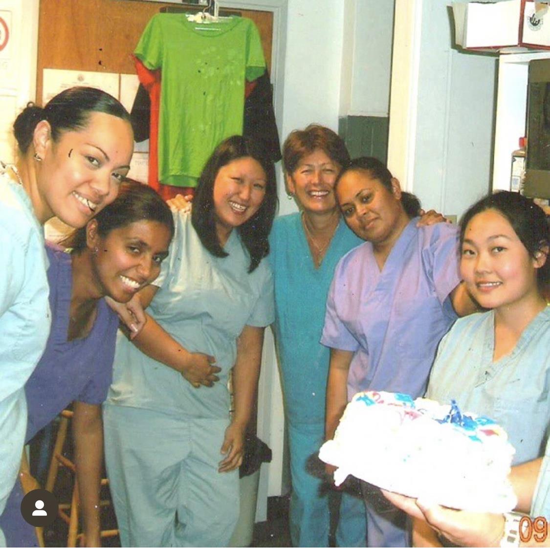 A group of women in scrubs holding a cake