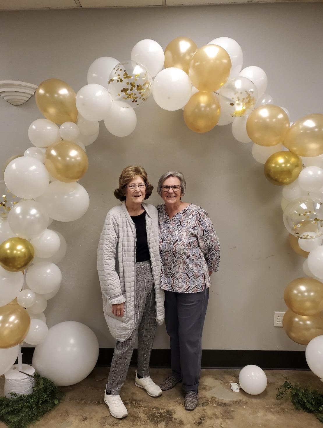 Two women standing in front of a balloon arch