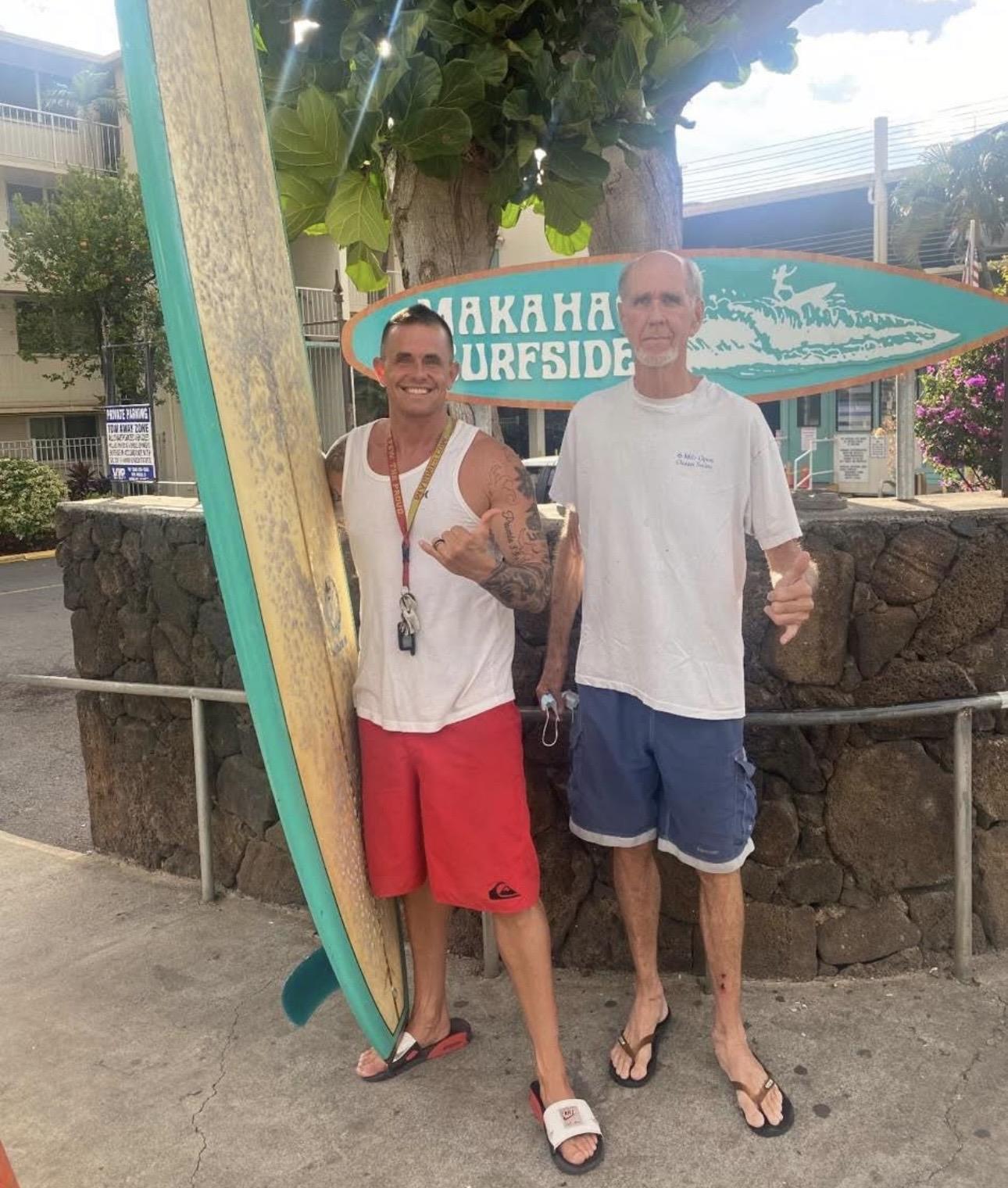 Two men standing next to a surfboard