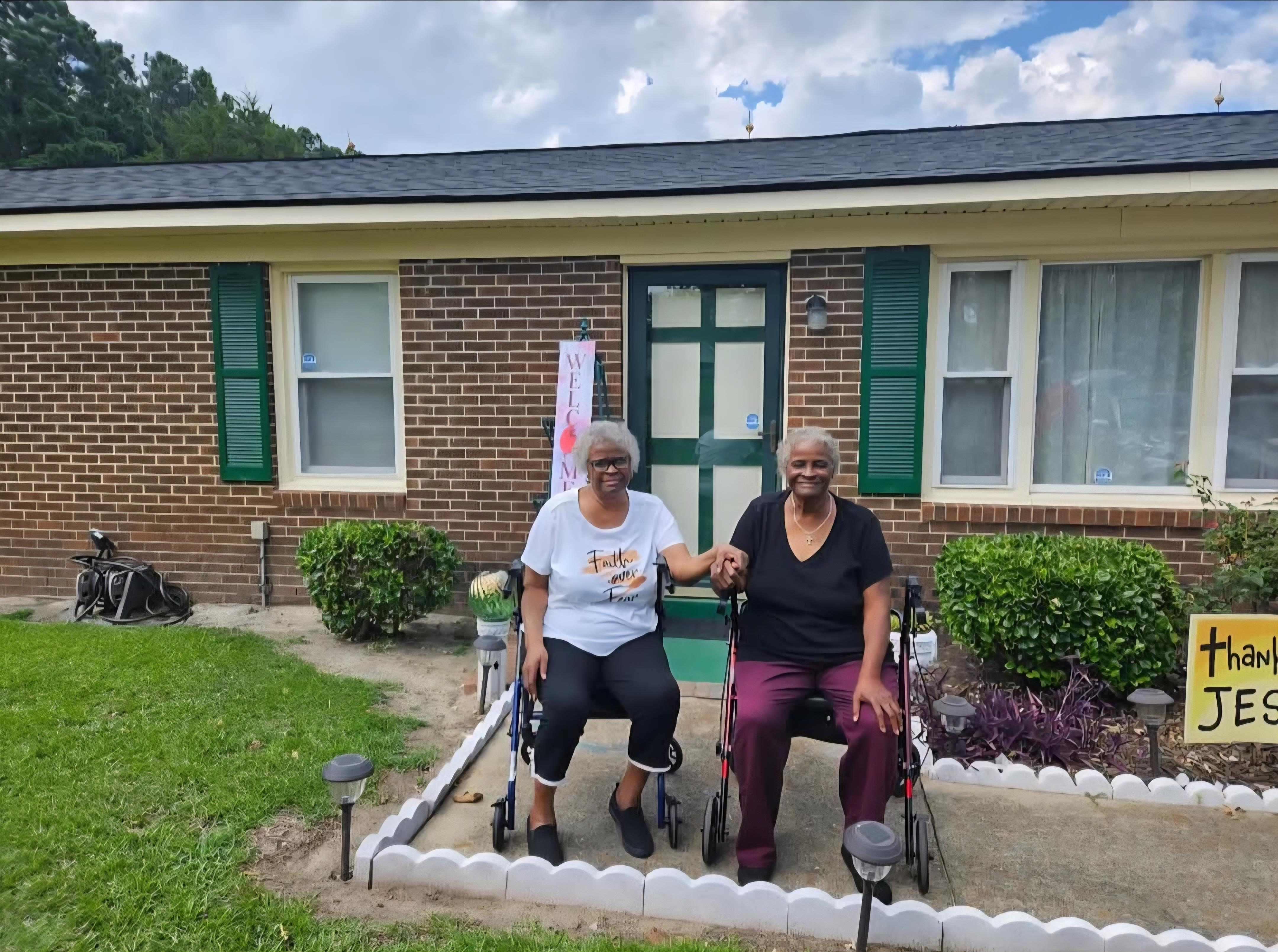Two women sitting in wheelchairs in front of a house