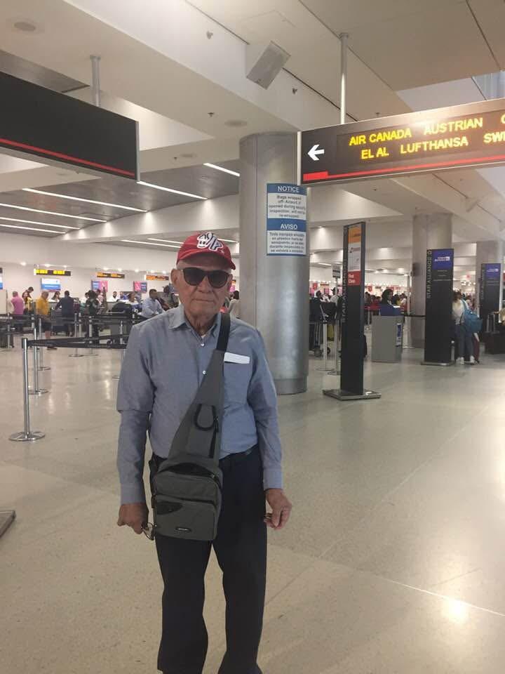 An old man in a red hat and sunglasses standing in an airport