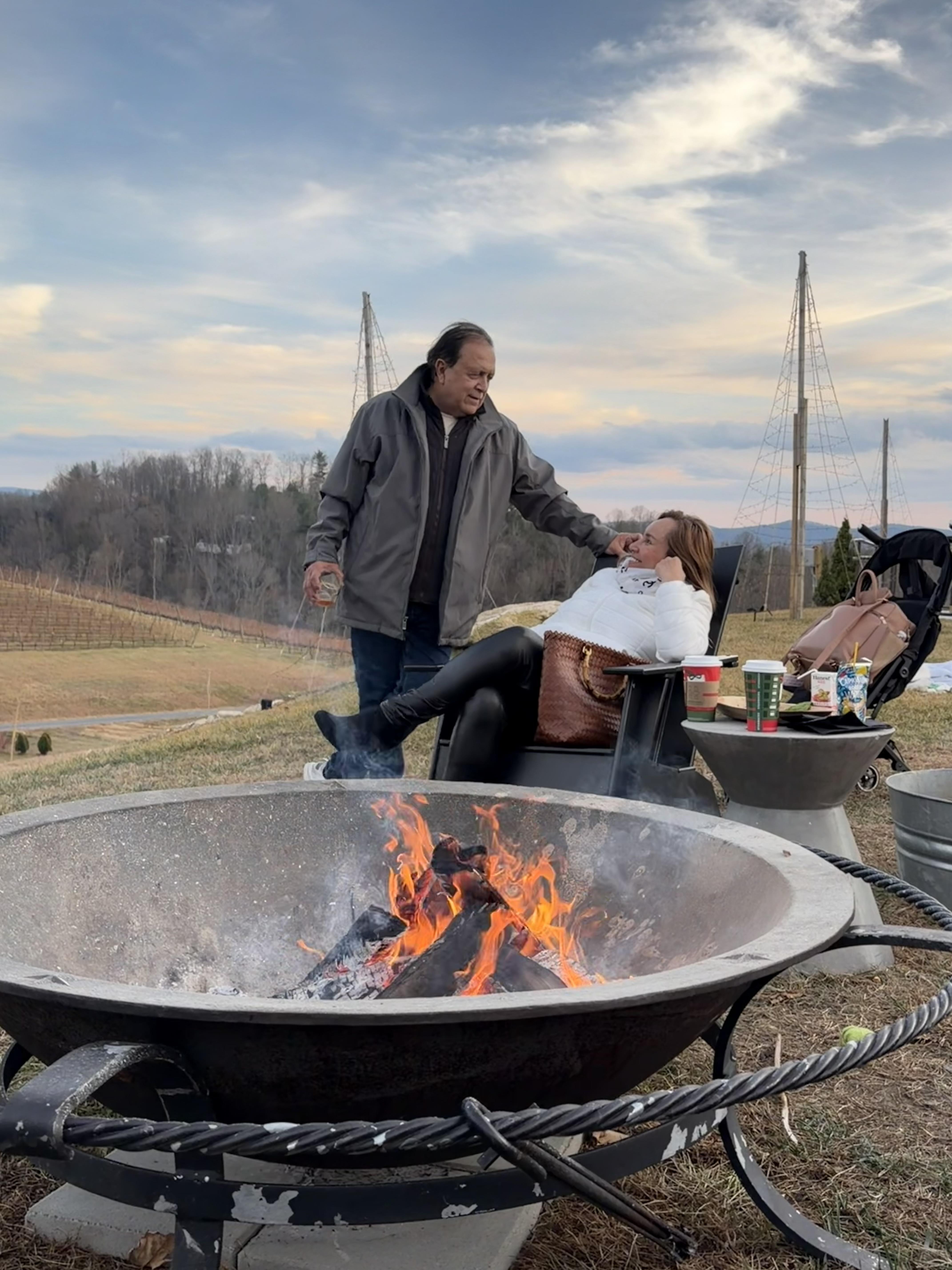 A man and woman sitting in a chair by a fire pit