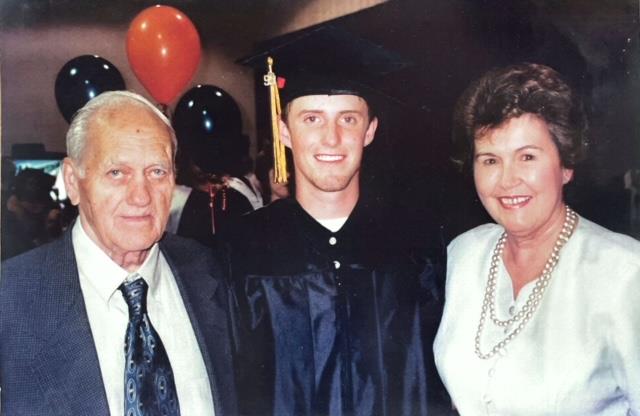 A man in a graduation gown and cap with his parents