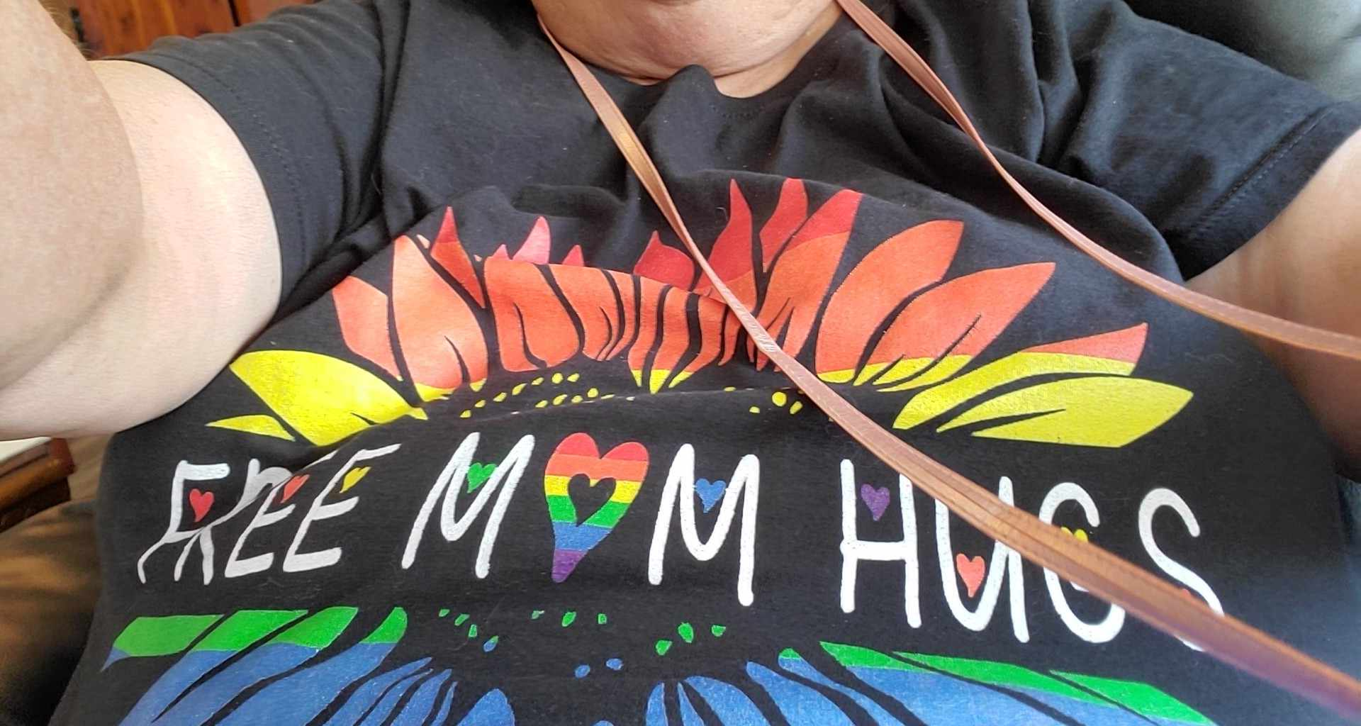 A person wearing a black shirt with a rainbow sun and text