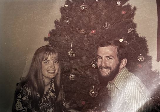 A man and woman sitting next to a christmas tree
