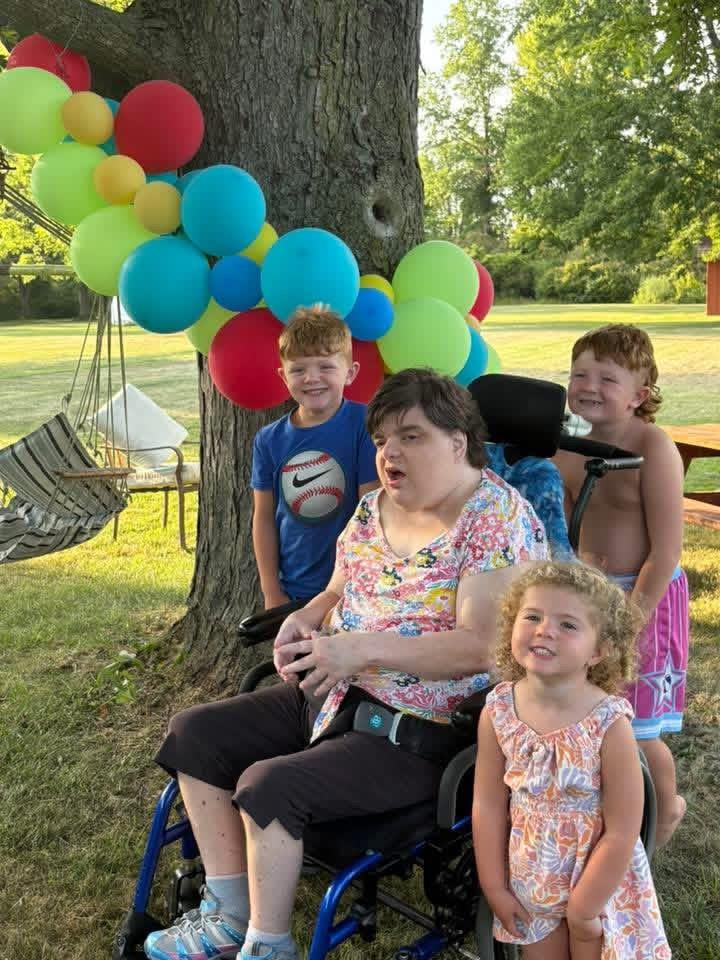 A woman in a wheelchair with children in front of a tree