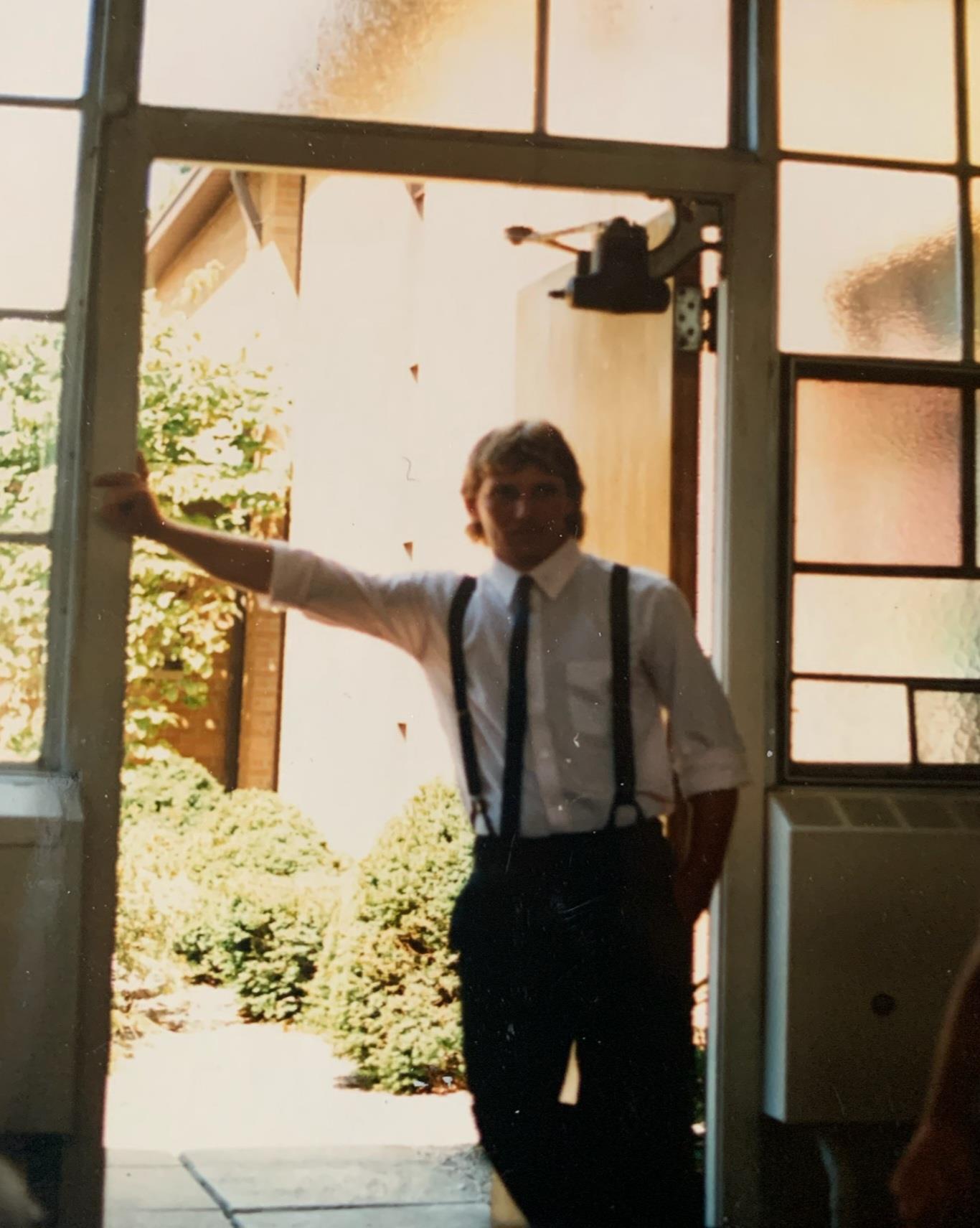 A man in suspenders and tie standing in front of a door