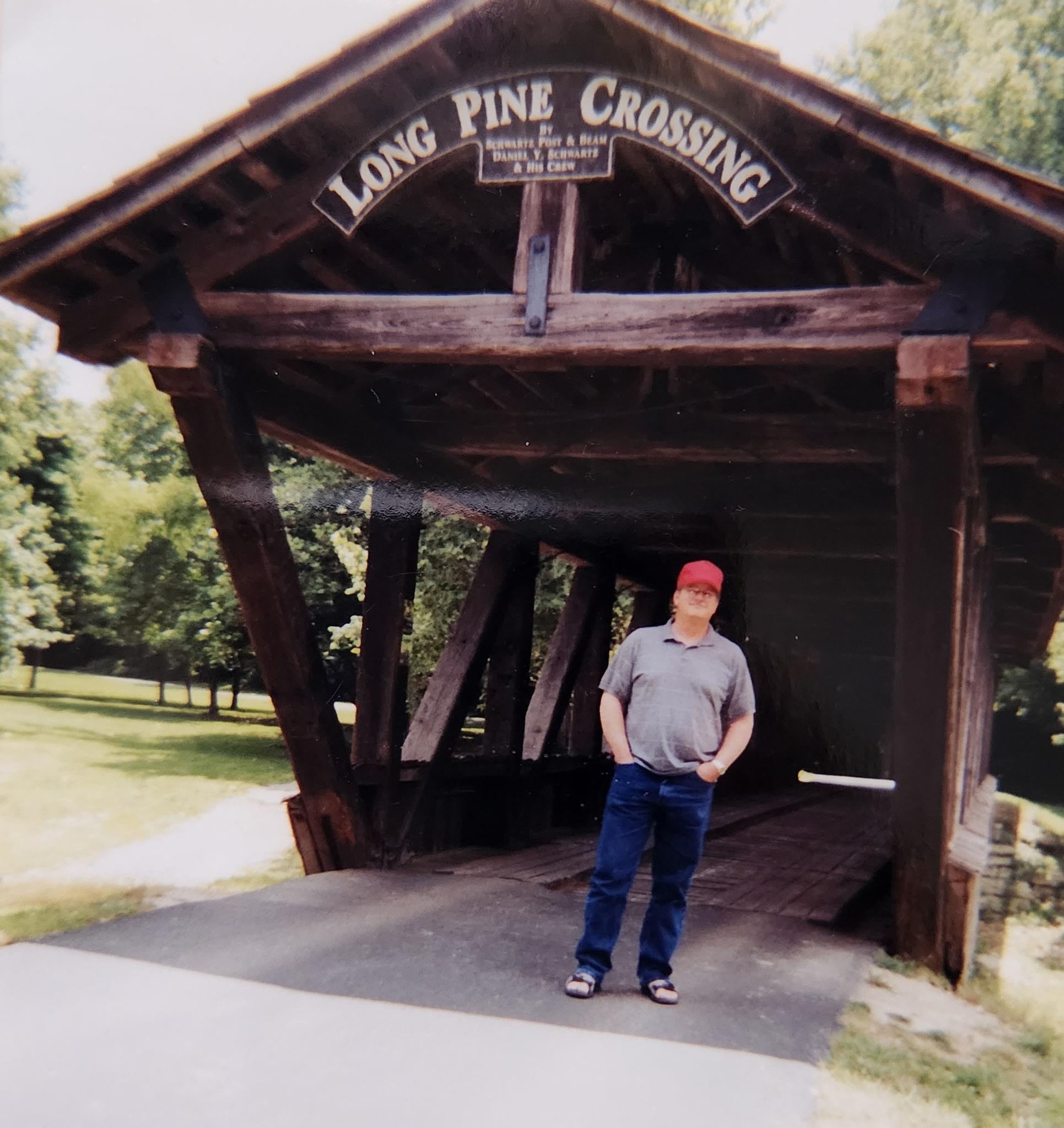 A man standing in front of a covered bridge