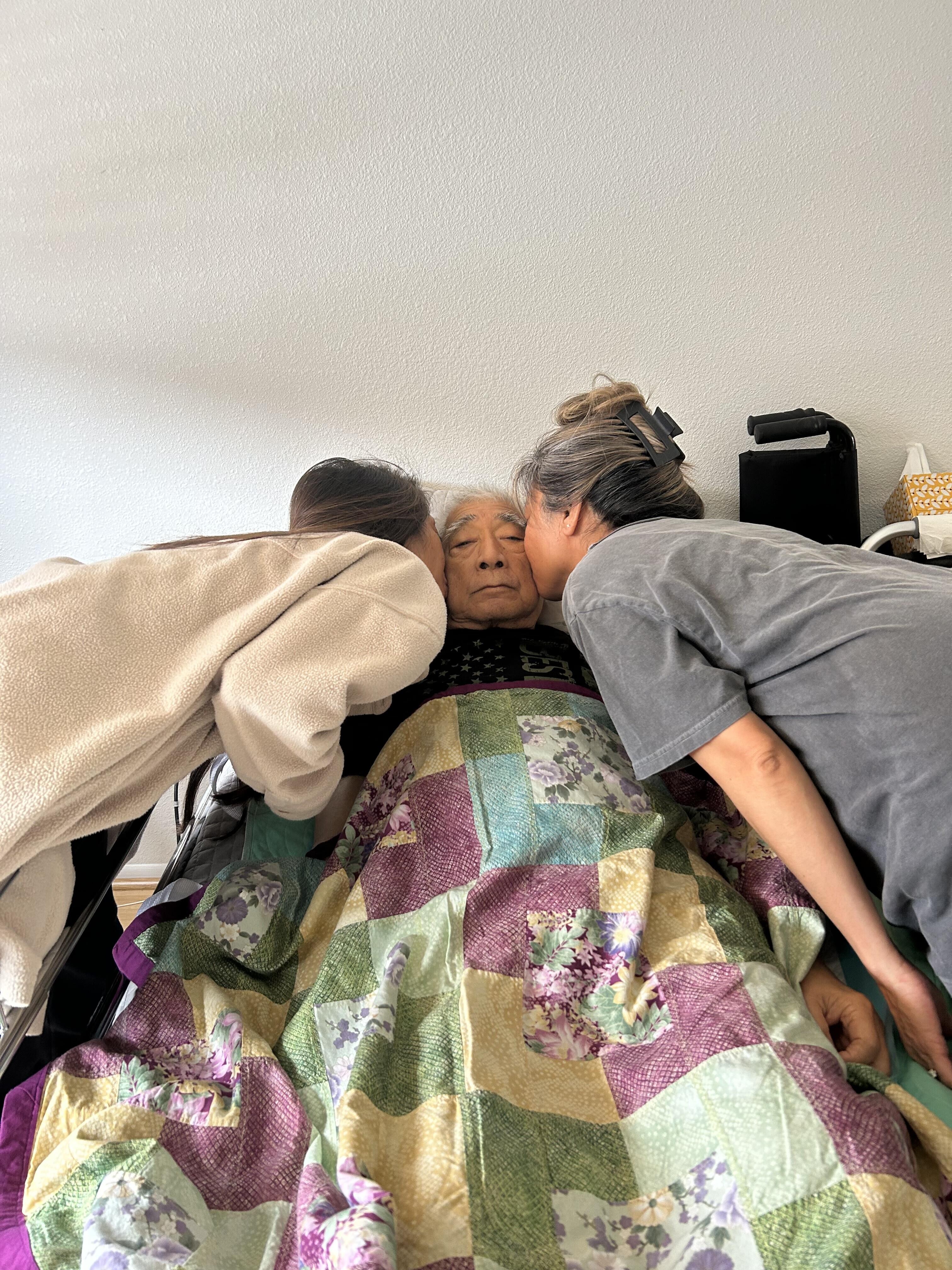 A woman kissing an old woman in a hospital bed