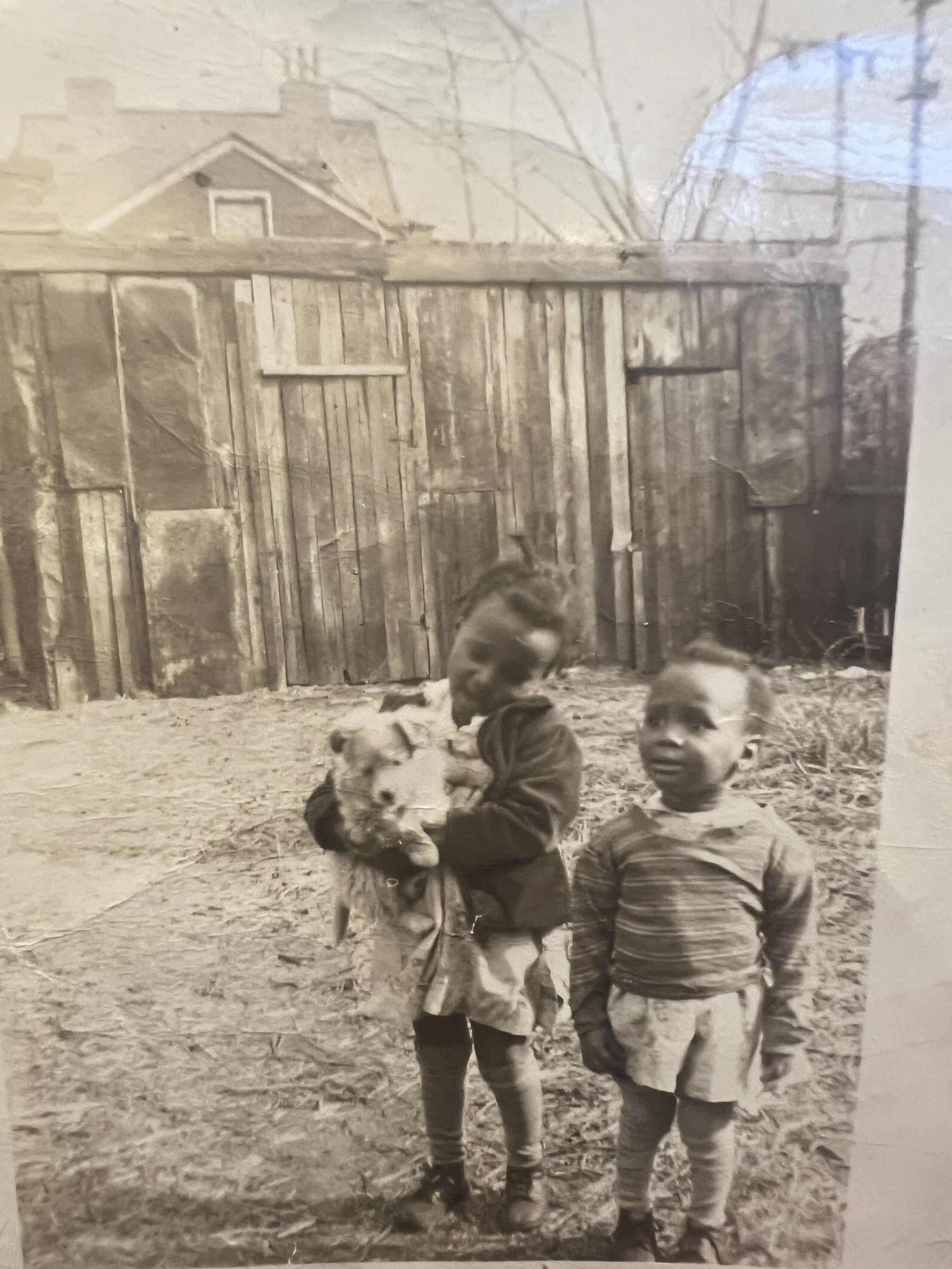 A black and white photo of two children holding a dog