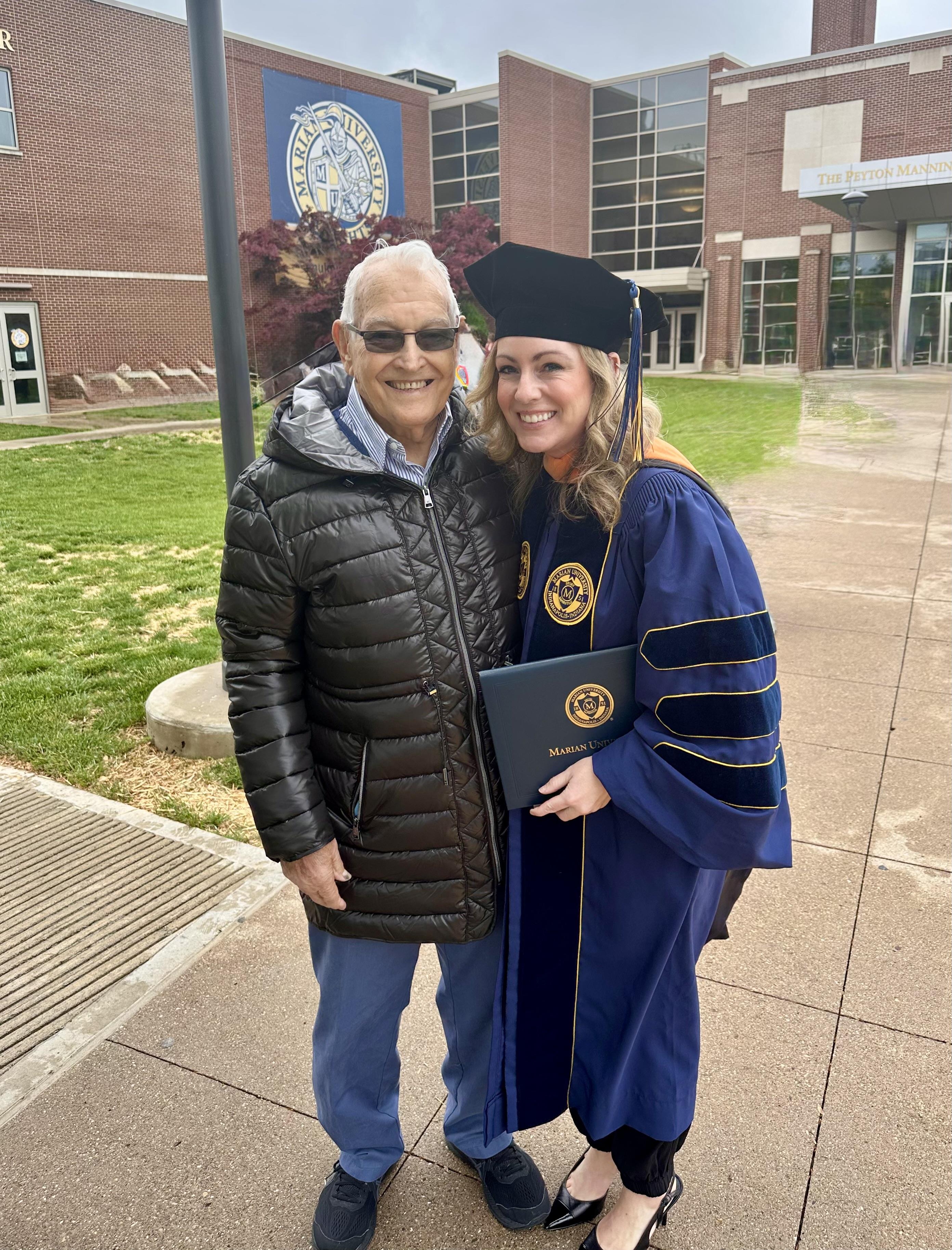 A woman in a graduation cap and gown standing next to an old man