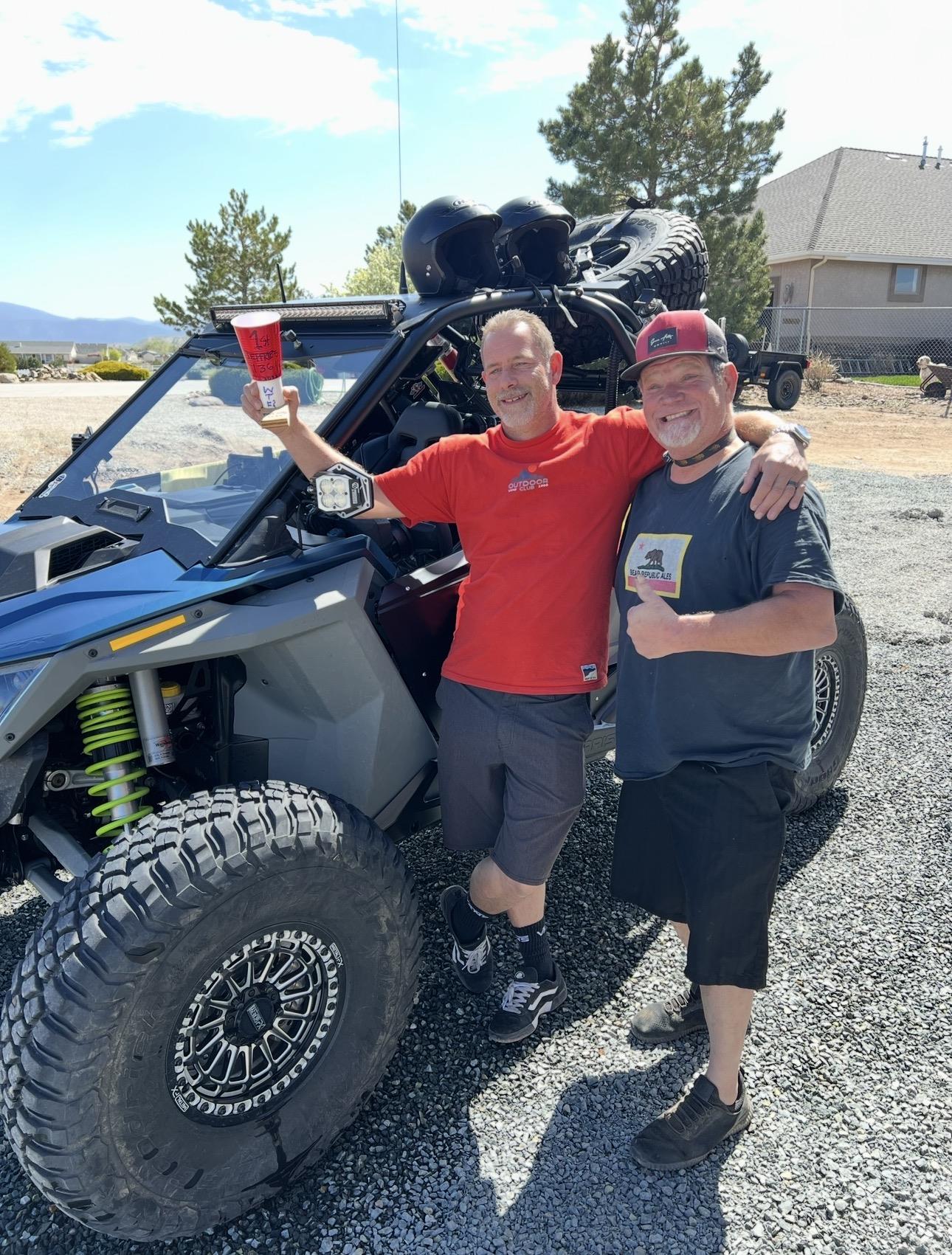 Two men holding up cups and standing next to a vehicle