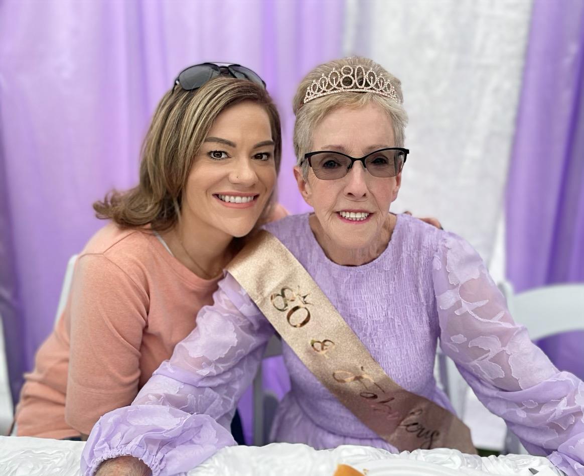 A woman with a sash and crown sitting next to another woman
