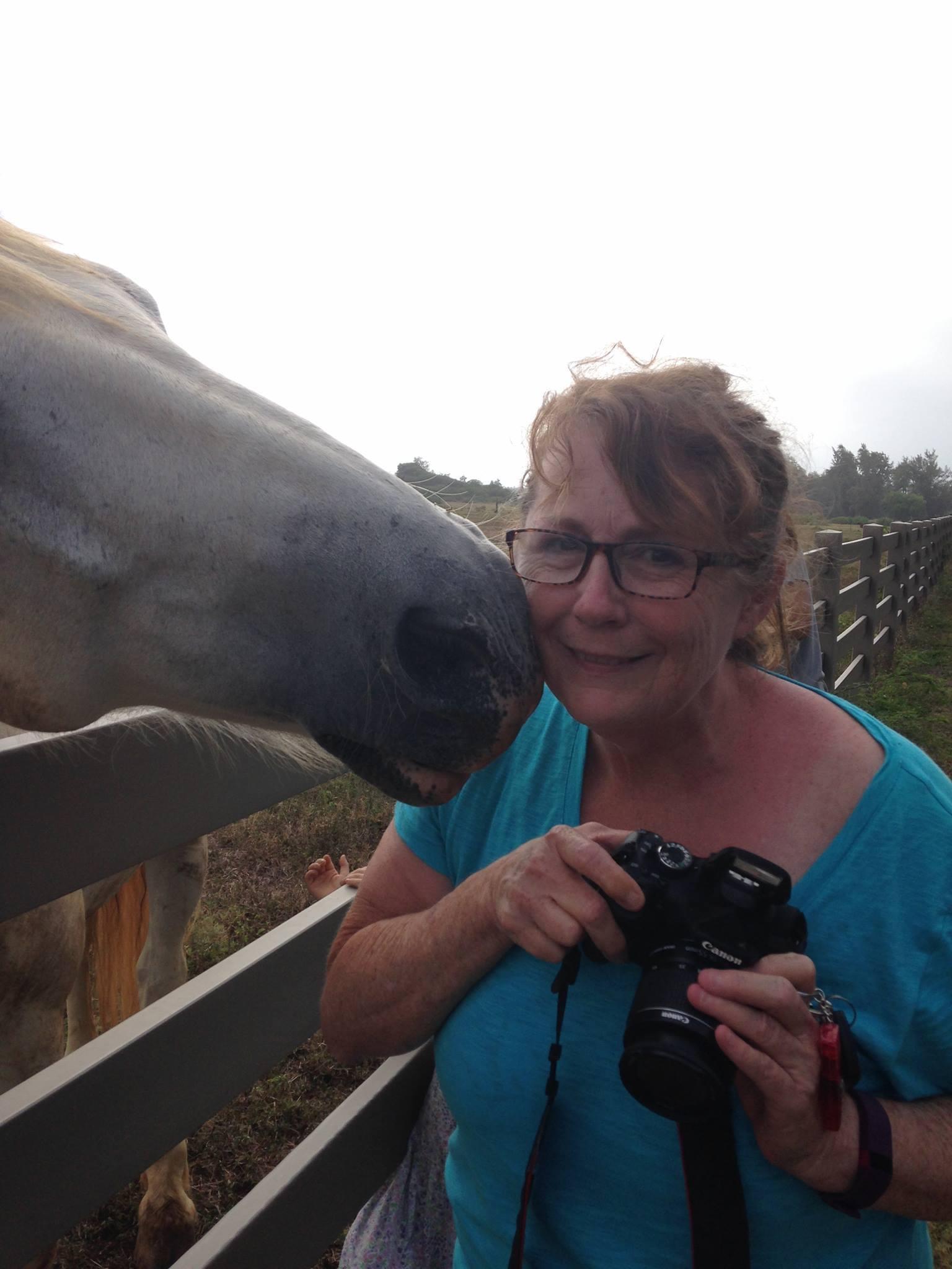 A woman holding a camera next to a horse